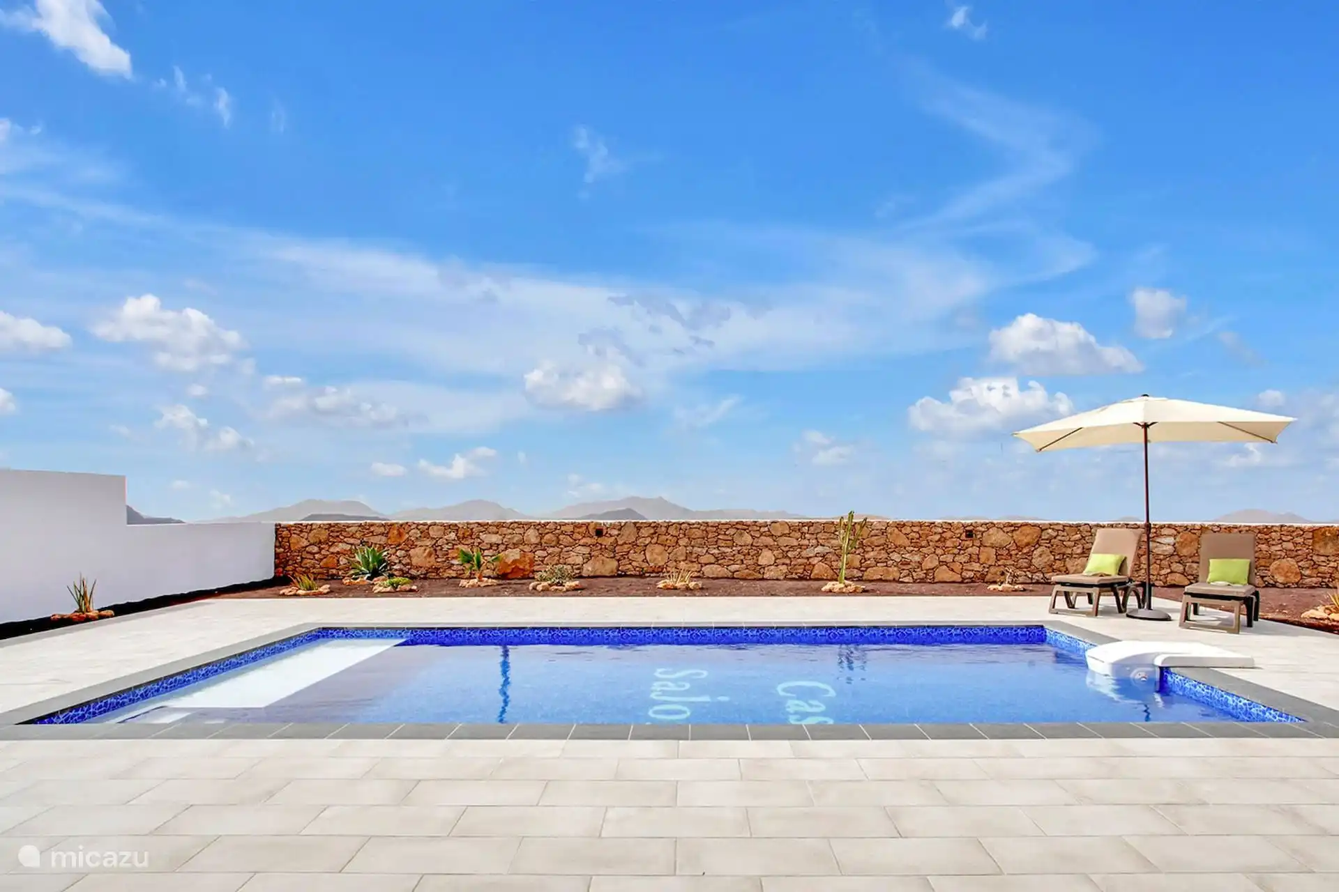 La piscina desde el otro extremo, con el muro de piedra seca, los cactus del jardín y las montañas al fondo.