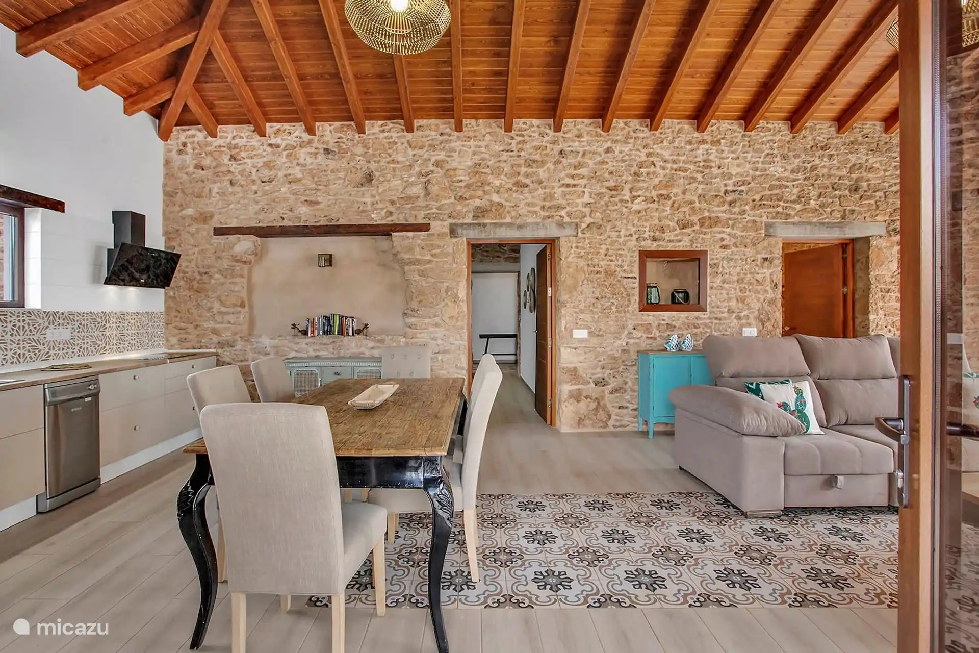 Cocina abierta al comedor y al salón, con lavavajillas y campana, sobre suelo hidráulico y bajo el techo de madera.