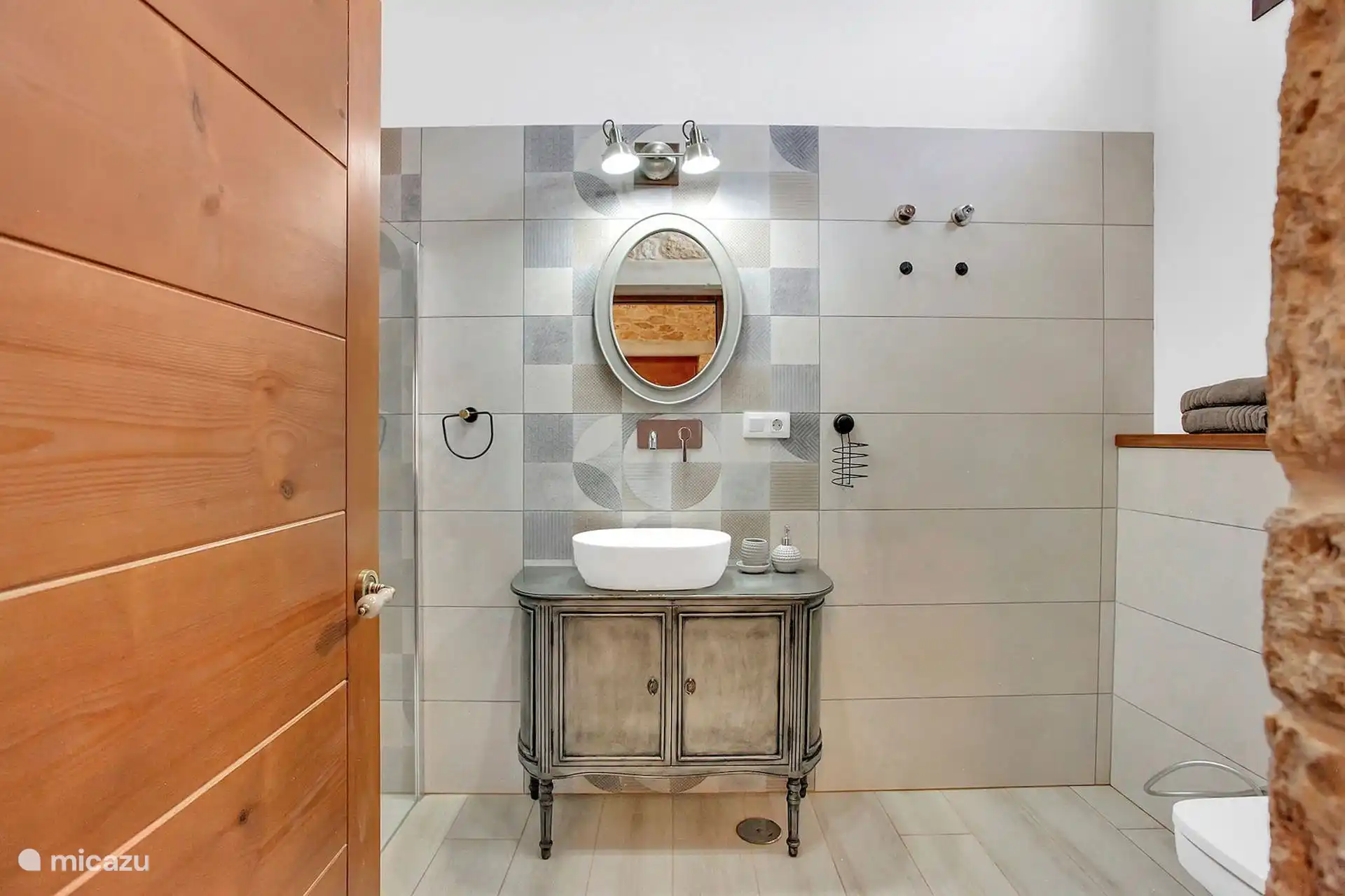 Baño con lavabo sobre mueble antiguo, espejo ovalado, azulejo geométrico y mampara de ducha a la izquierda.