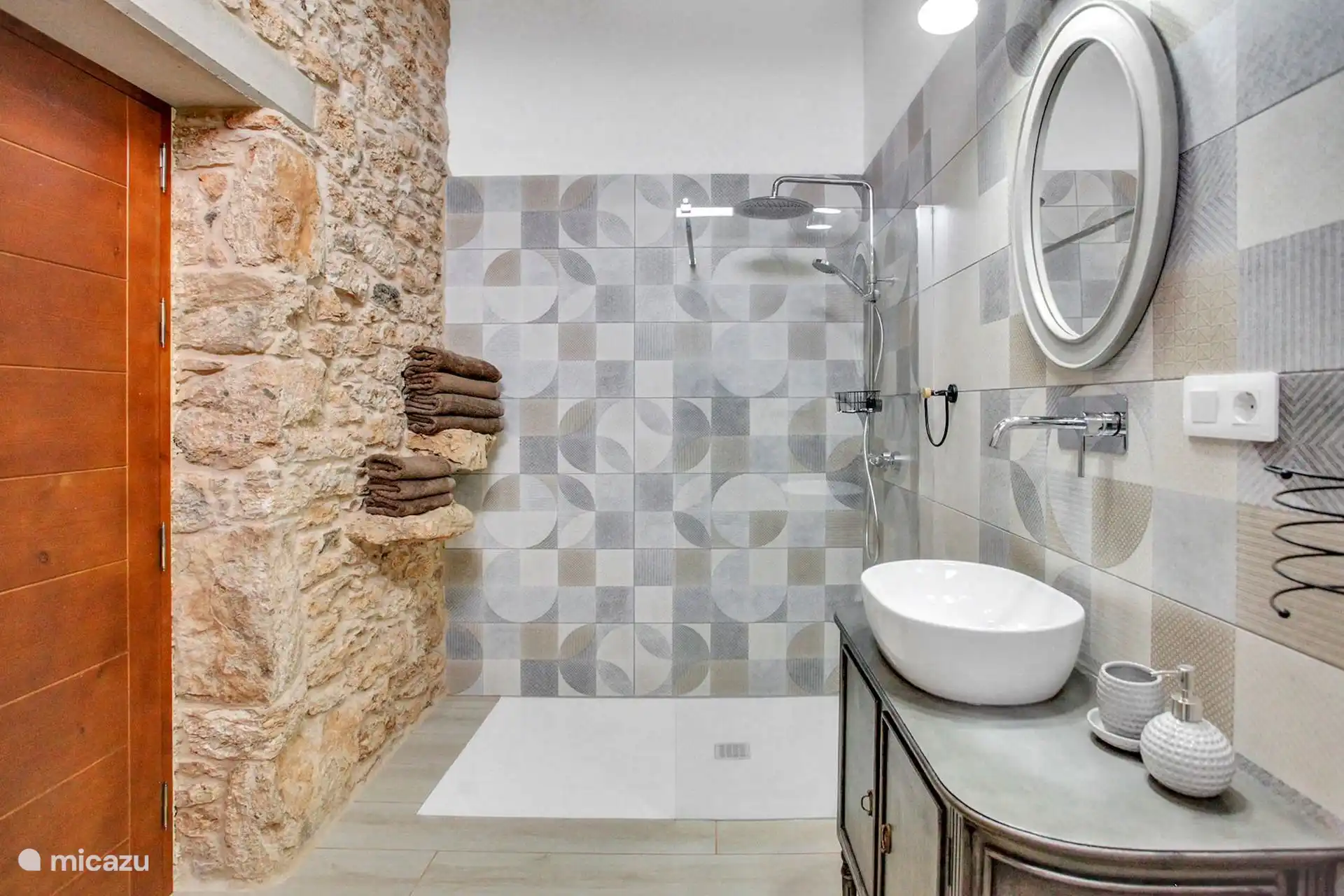 Ducha a ras de suelo con rociador y toallas sobre la repisa de piedra; a la derecha, el lavabo sobre el mueble.