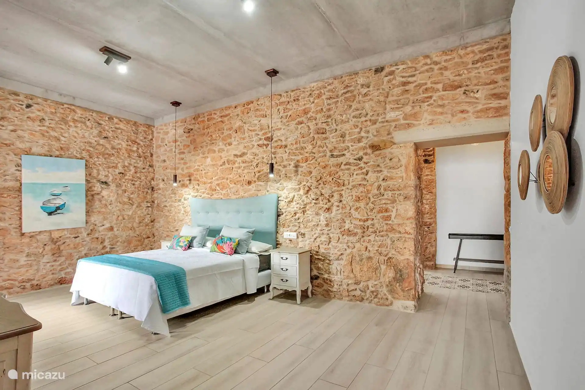 Otra vista del mismo dormitorio, con cuadro de barcas y paso abierto a una zona con banco al fondo.