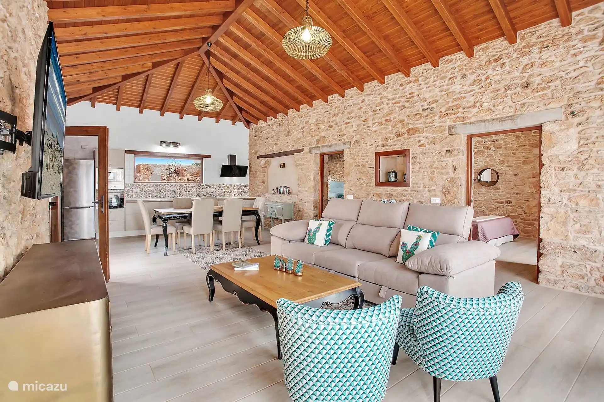 Otra vista del salón, con la mesa de comedor y la cocina al fondo, todo bajo el mismo techo de madera a dos aguas.