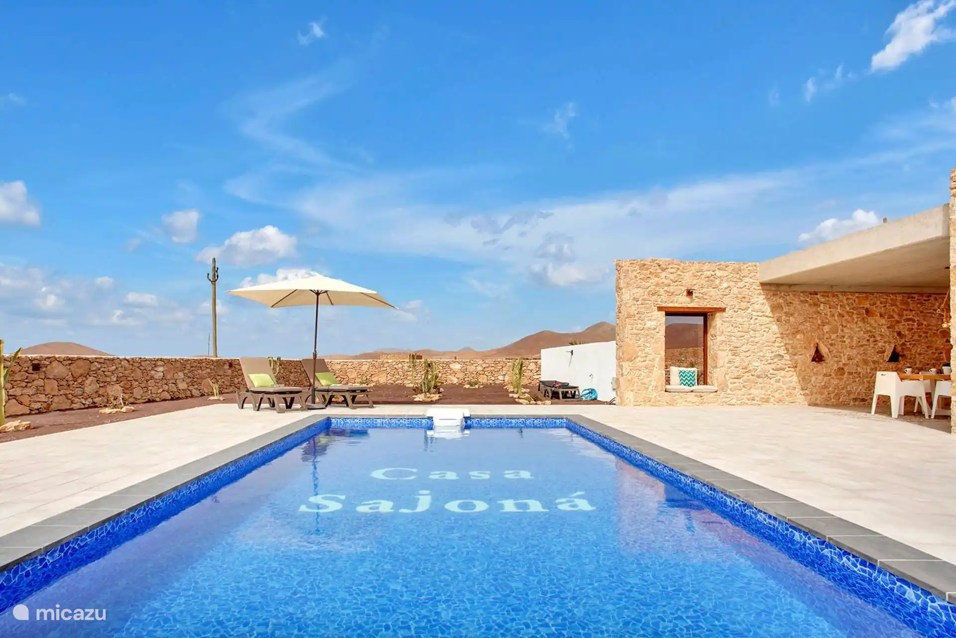 Otra vista de la piscina, con las tumbonas a la izquierda y el porche de piedra a la derecha.