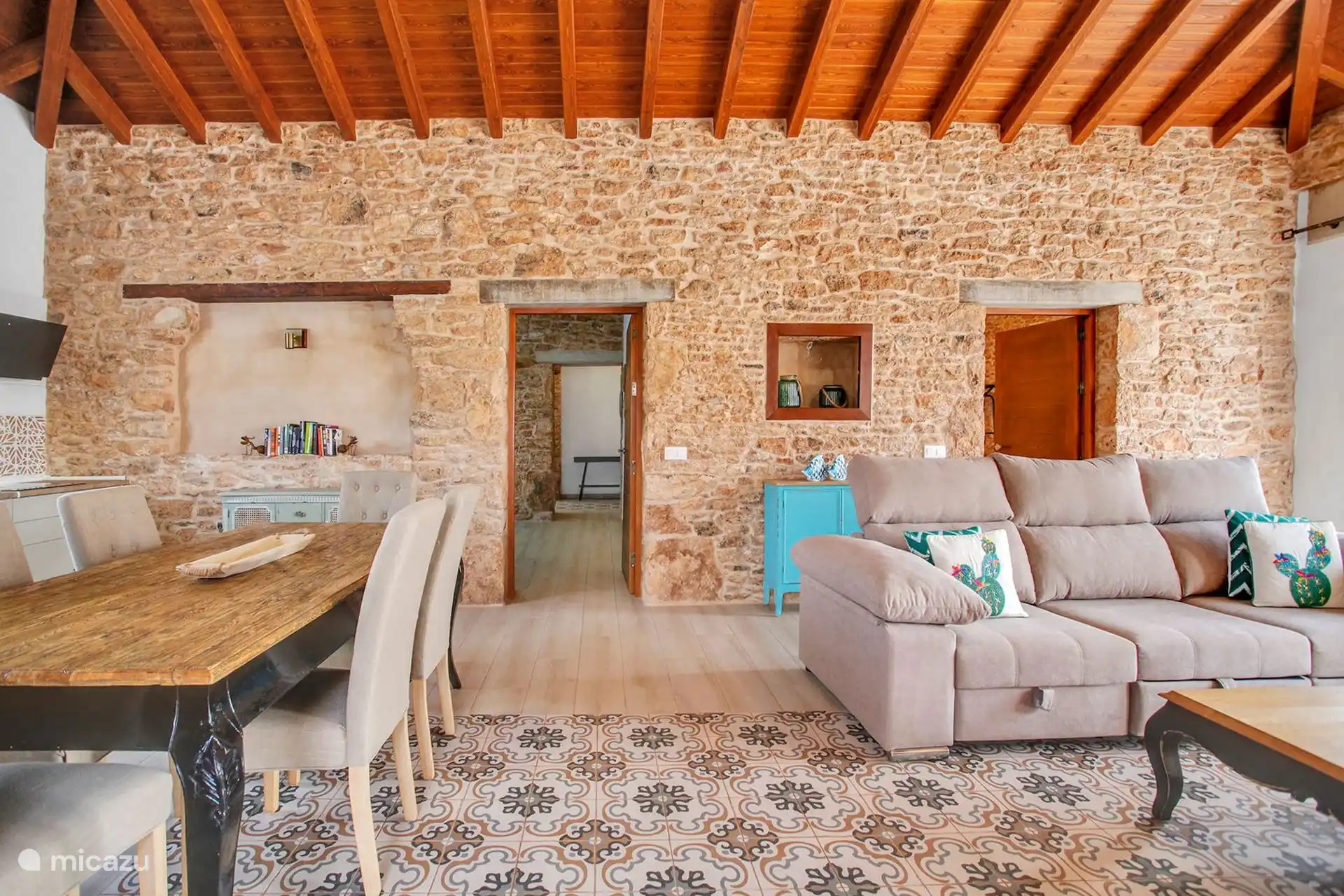 Zona de salón y comedor, con el sofá y el mueble turquesa contra la pared de piedra.