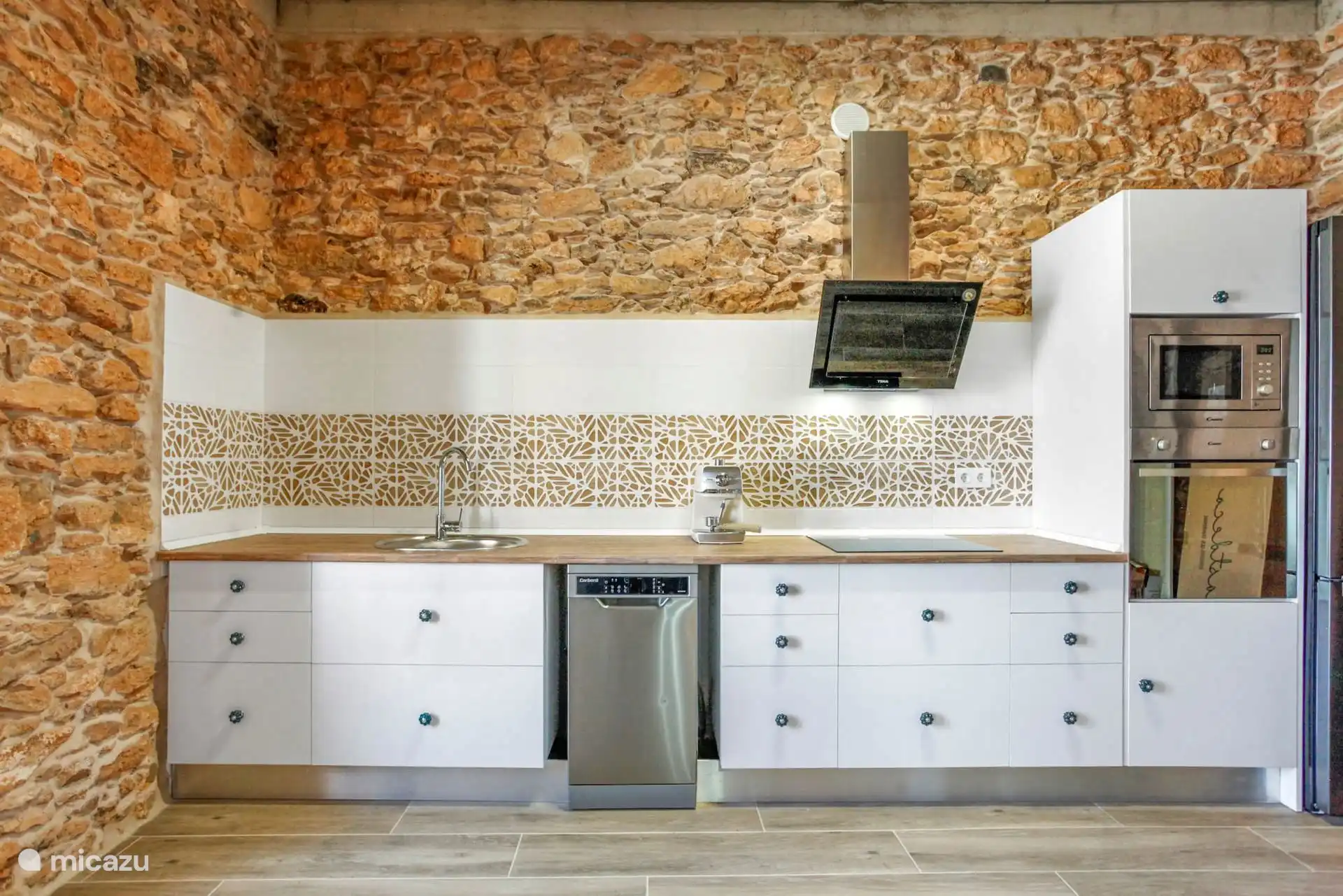 Keuken met houten aanrechtblad, gootsteen, keramische kookplaat, vaatwasser, oven en magnetron, onder de stenen muur.