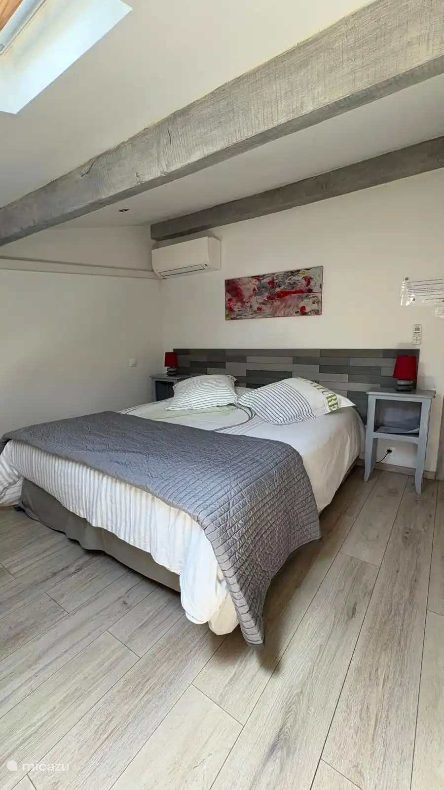 Visualize this air-conditioned room under the roof, combining the charm of exposed beams with the modern comfort of a large double bed.