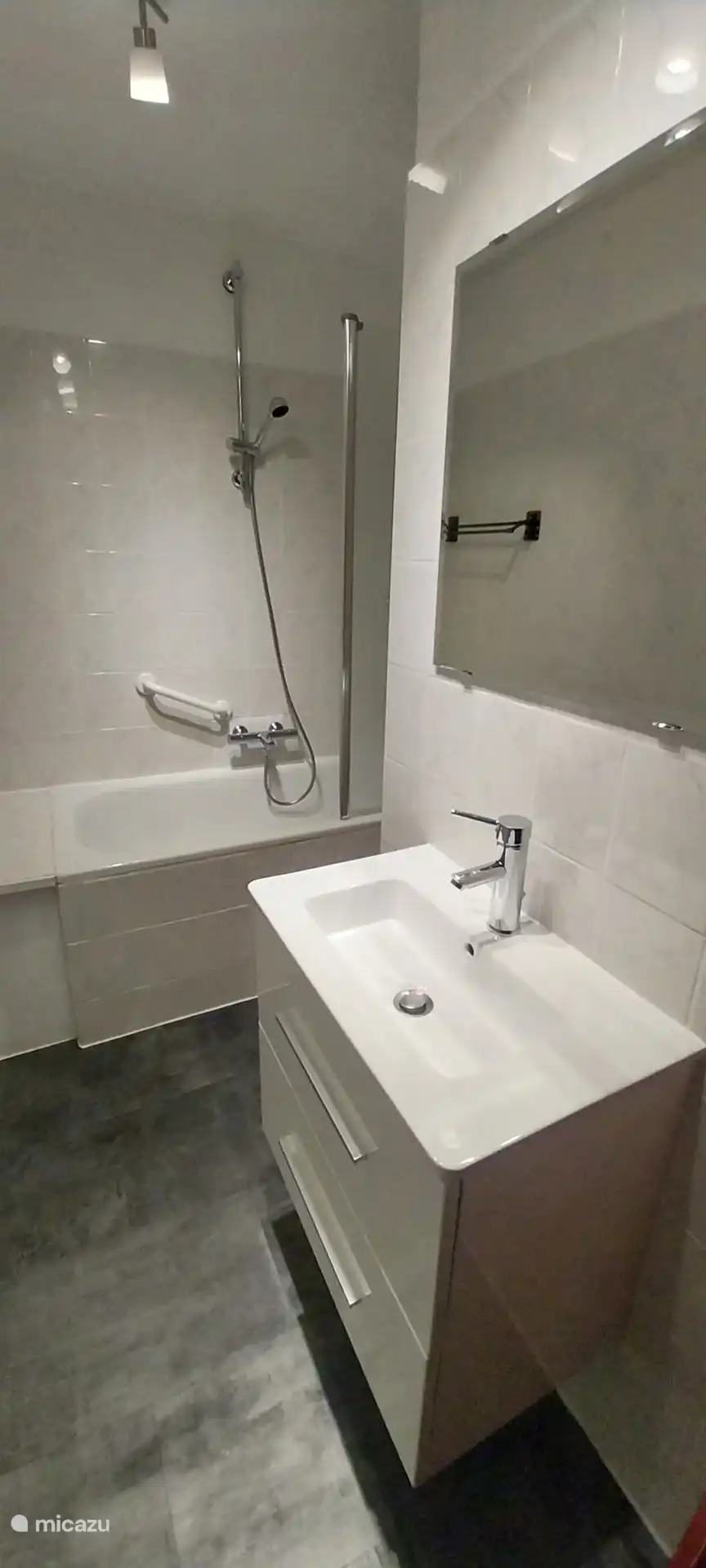Bright and modern bathroom equipped with a bathtub with grab bar, a hand shower and a stylish vanity unit.