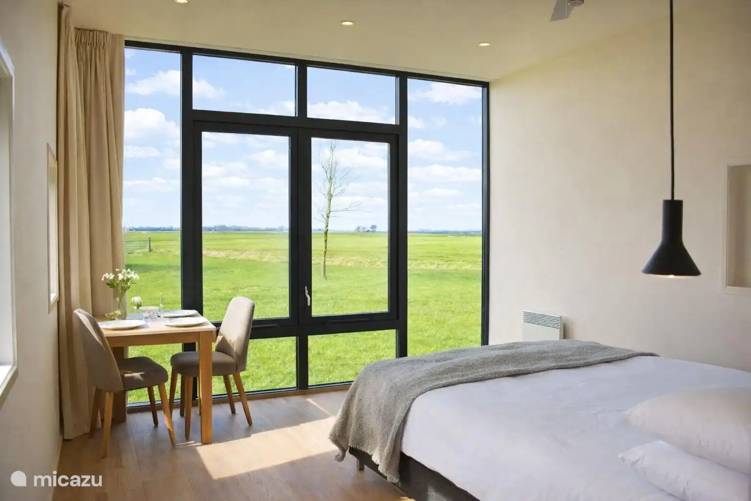 Licht en luchtig interieur met bed en eettafel aan het grote raam