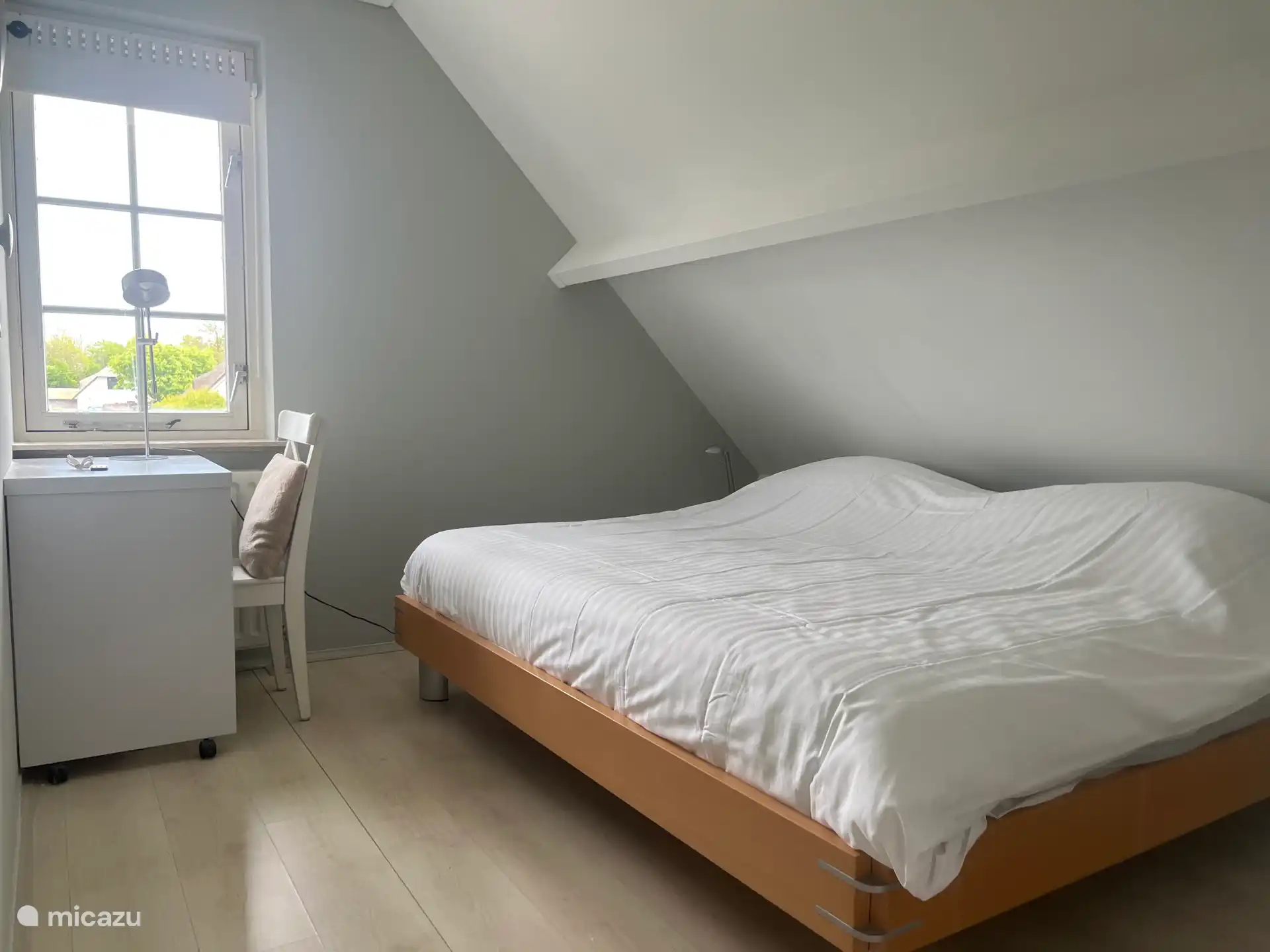 Tercer dormitorio con cama king size, escritorio, mesitas de noche y cómoda. Al pie de la cama, la pared está inclinada.