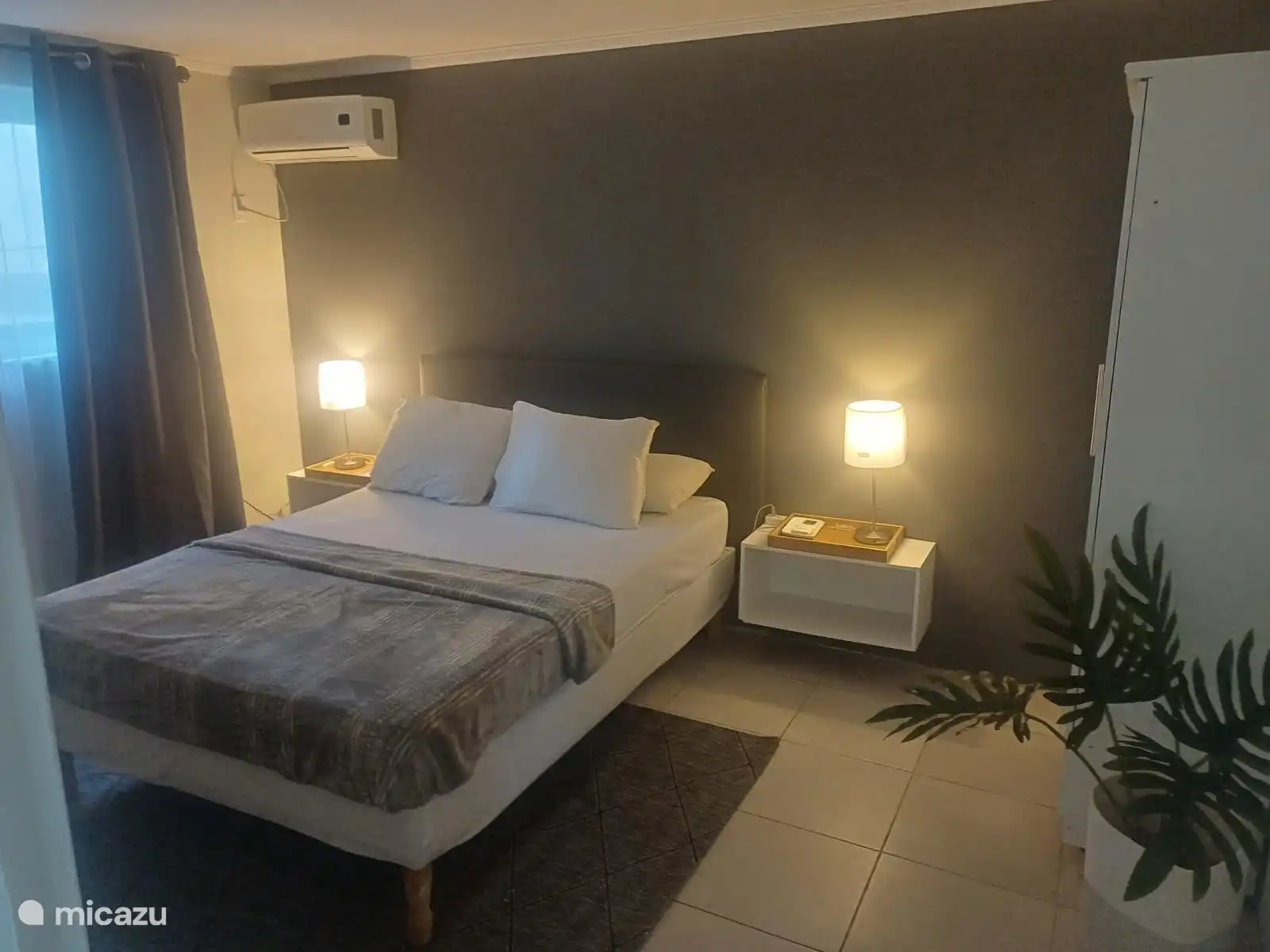 Lavandería con cama matrimonial cómoda, ropa de cabecera limpia, iluminación ambiental y aire acondicionado. Un espacio tranquilo y con estilo donde puedes relajarte y disfrutar de tu sueño nocturno