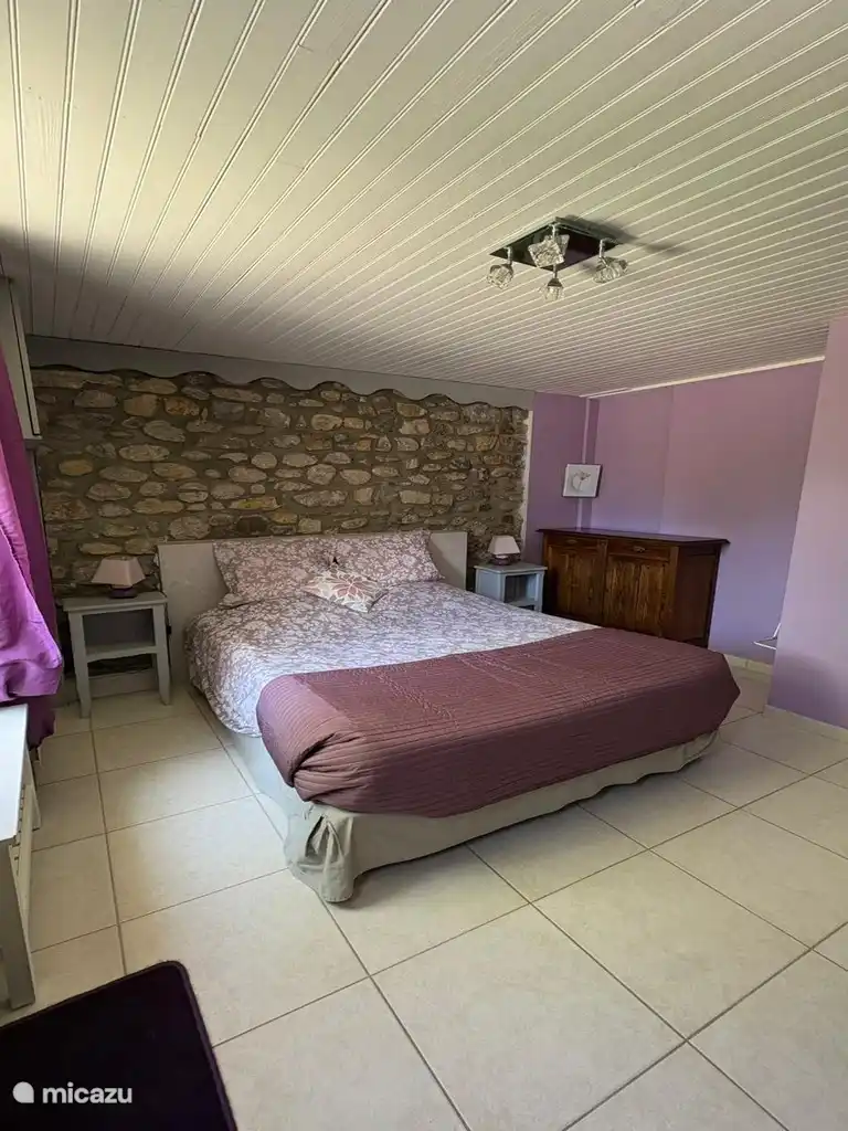 Ruime kamer met authentieke charme met een tweepersoonsbed, een muur van natuurstenen en warme decoratie.