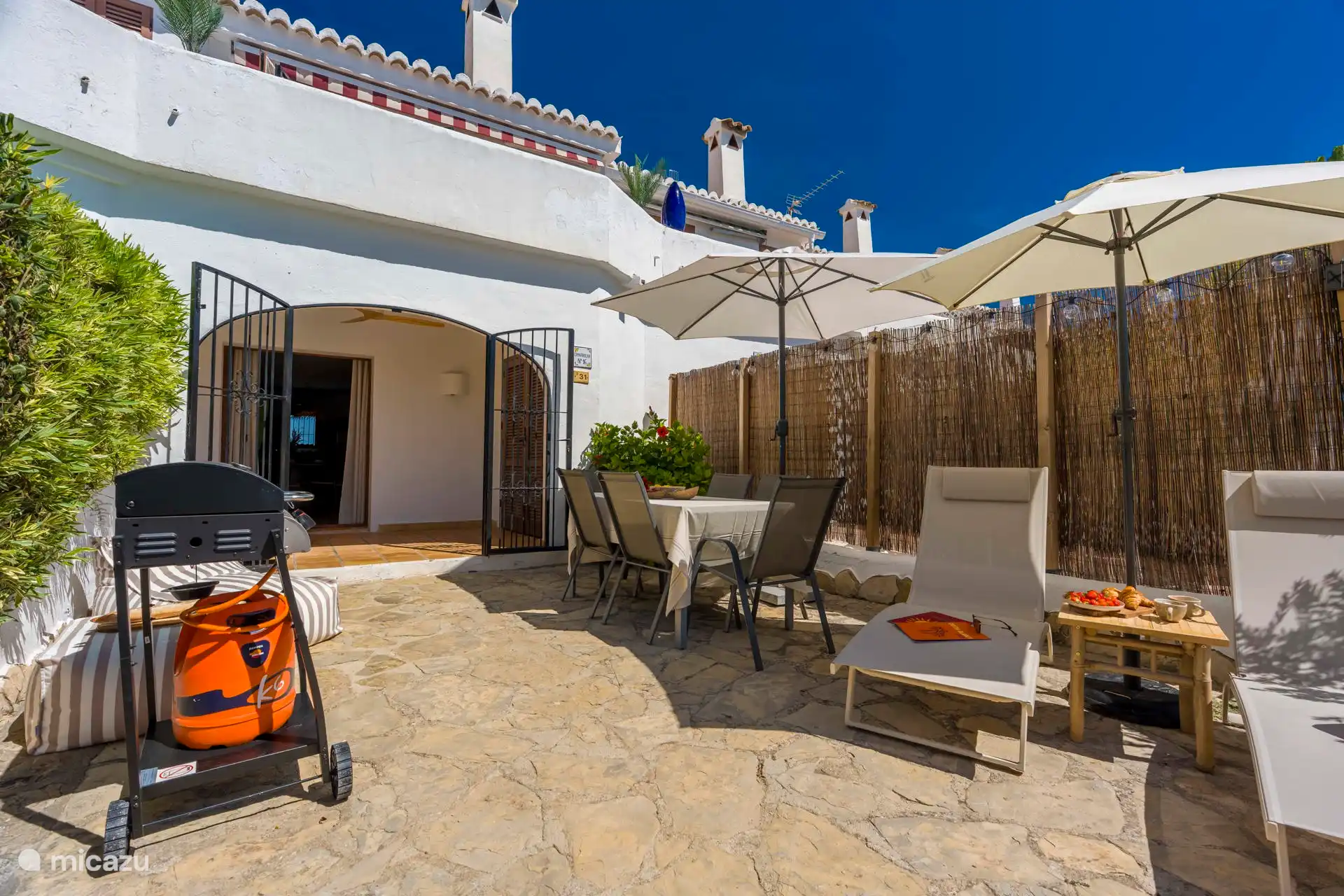 Der Garten mit Sonnenliege, Esstisch, Sonnenschirmen und einem abschließbaren Tor