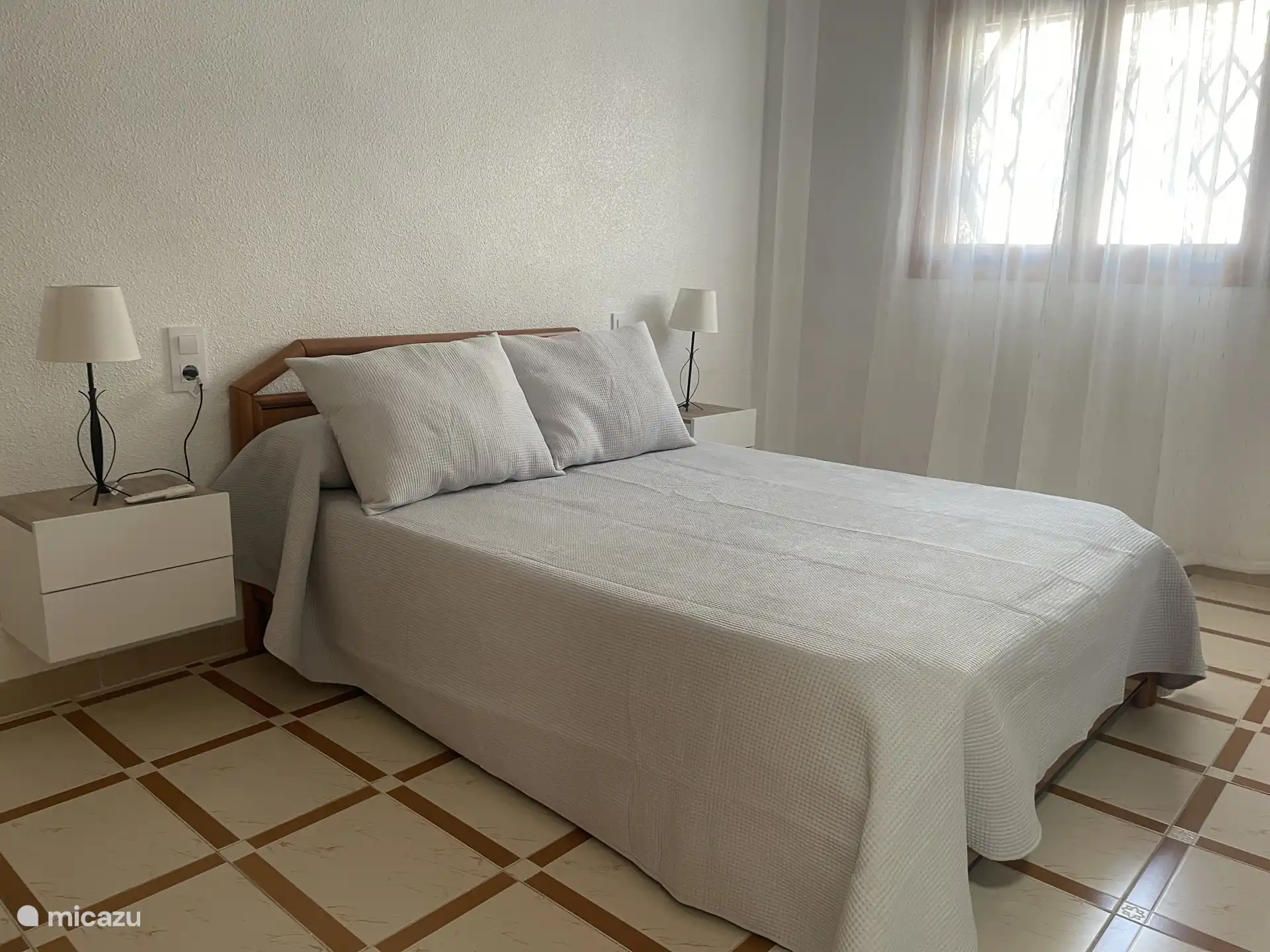 Chambre parentale avec lit double, tables de chevet et lumière naturelle.