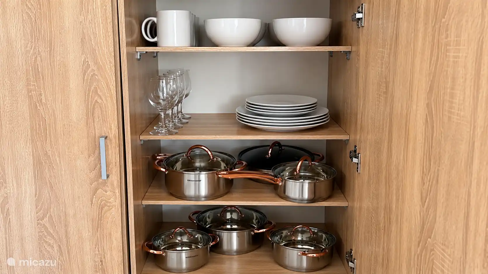 Ruime kast gevuld met servies, glazen en kookpotten. Alles aanwezig om eenvoudig zelf te koken en te genieten van een maaltijd in je eigen tempo.