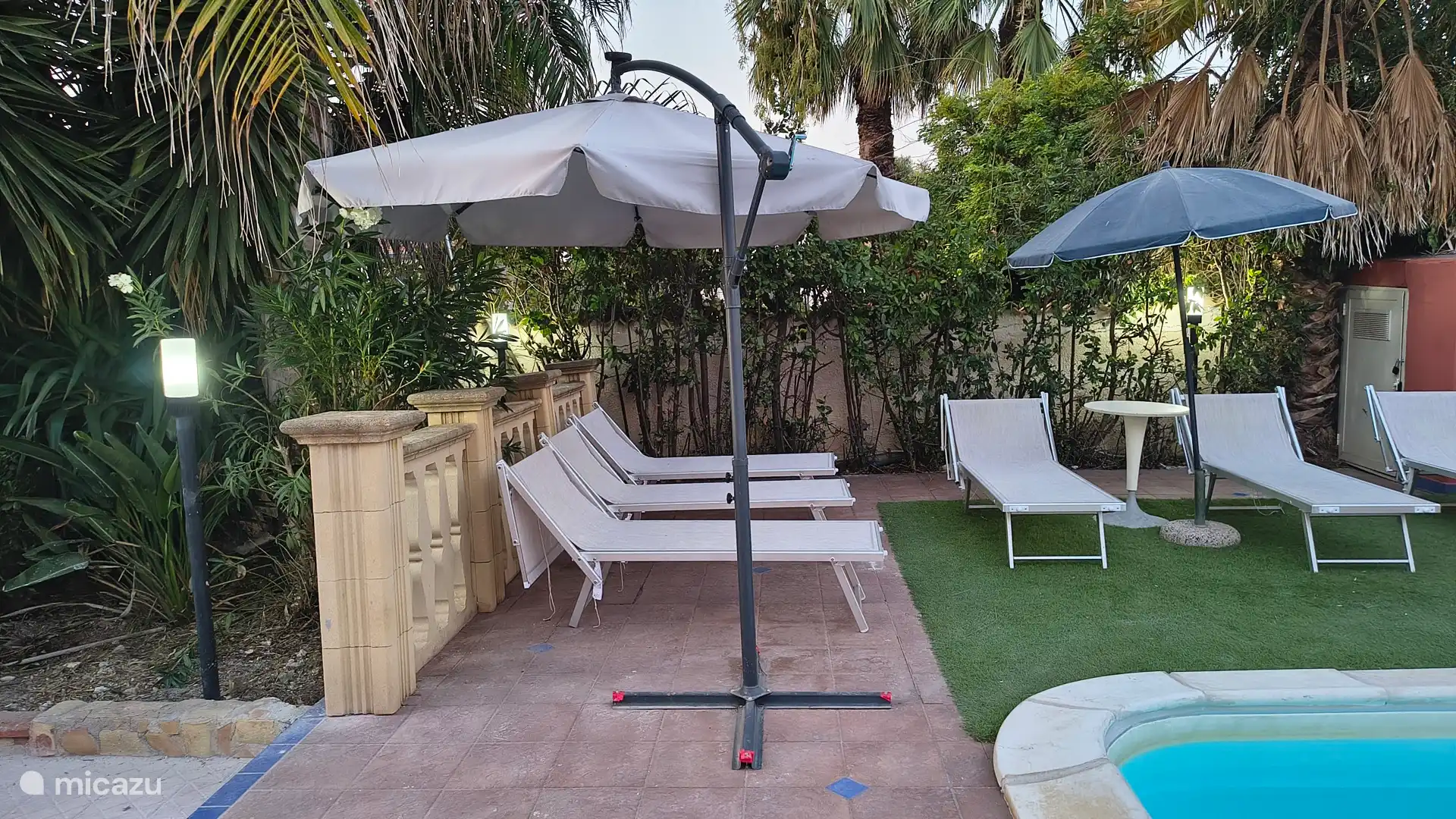 Ligbedden met parasol bij zwembad.