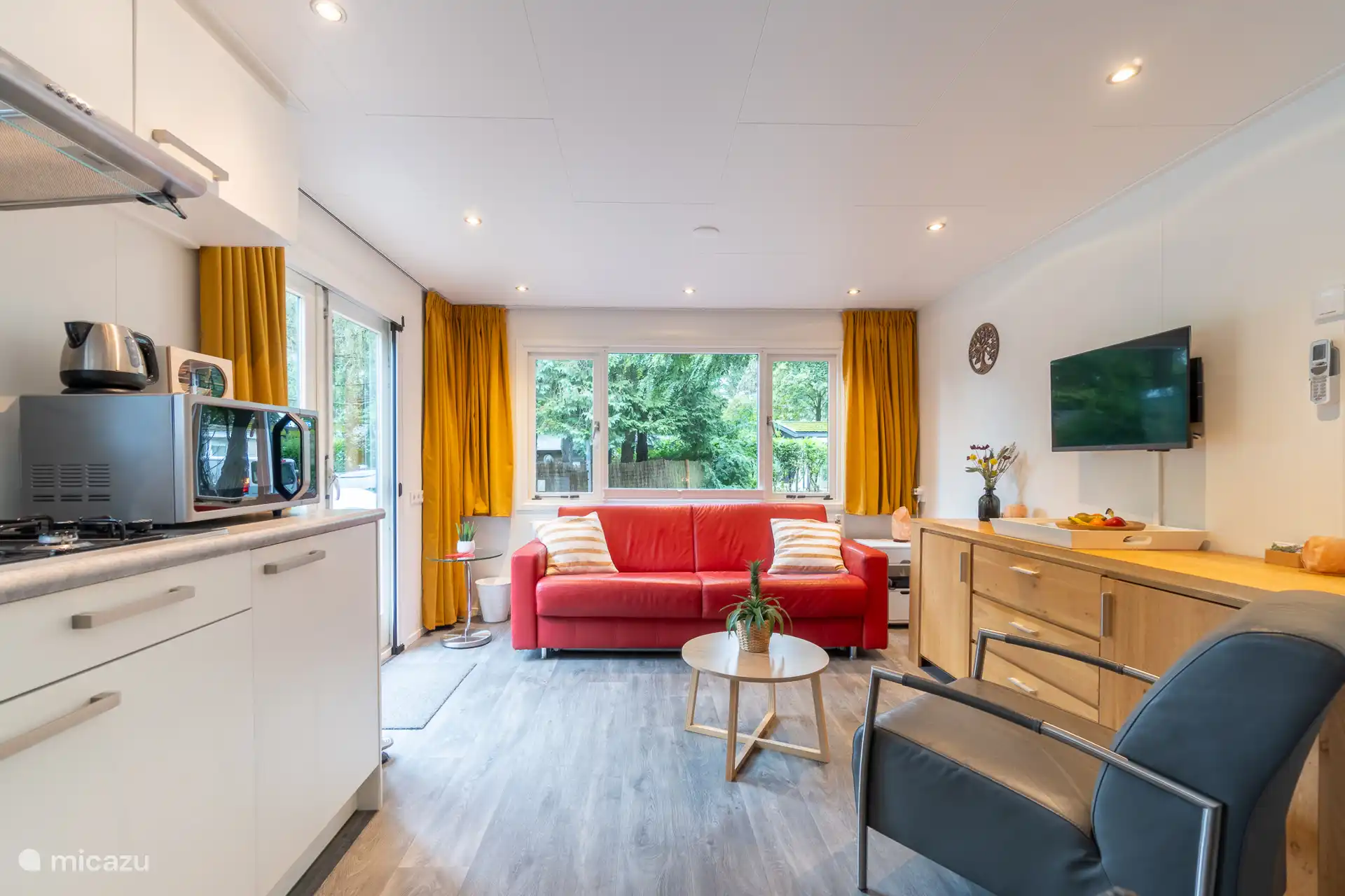 Sfeervolle woonkamer met comfortabele zithoek, Smart TV en een compleet ingerichte keuken.
