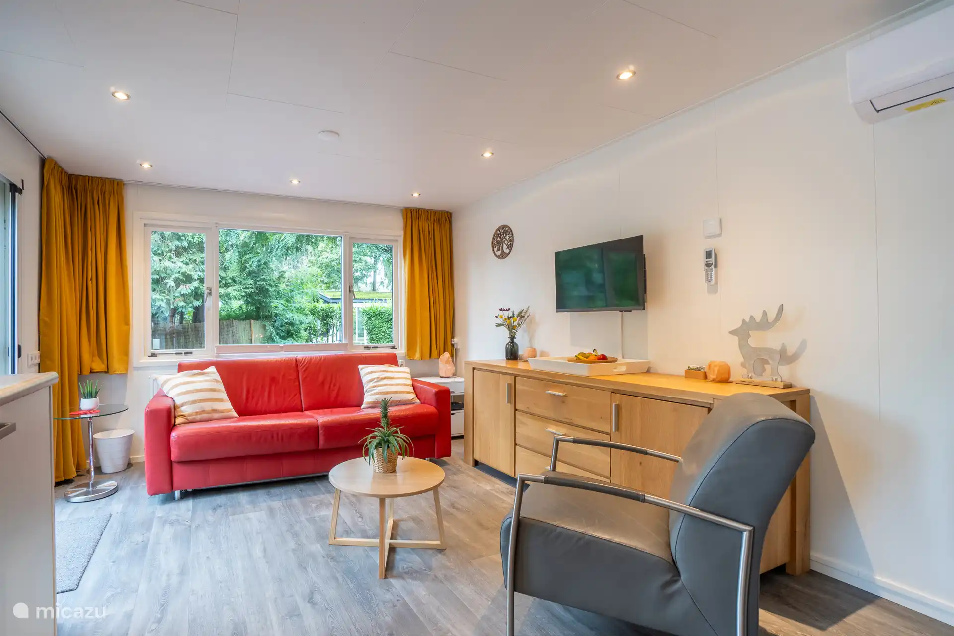 Sfeervolle woonkamer met comfortabele zithoek, eethoek, smart tv en uitzicht op de groene omgeving.