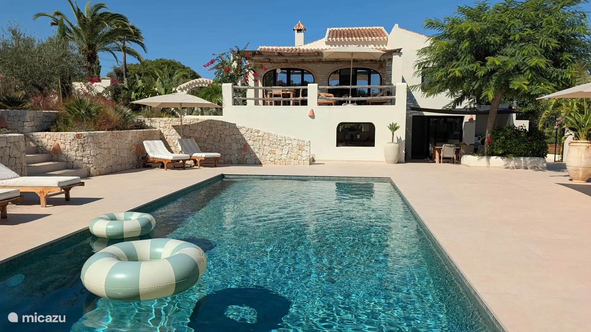 Zwembad met de villa op de achtergrond en ligbedden aan de rand. Eén stap vanaf het terras en je ligt al in het water.