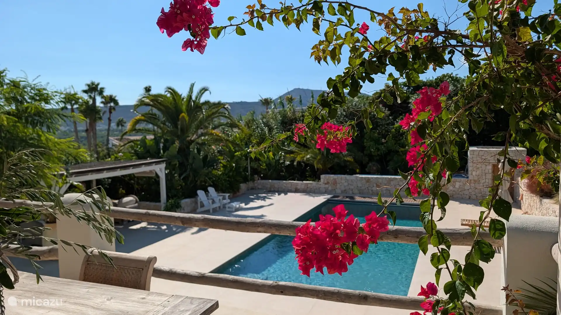 Bloeiende bougainville boven het zwembad, met palmen en heuvels op de achtergrond. Hier voel je meteen de mediterrane zomer.