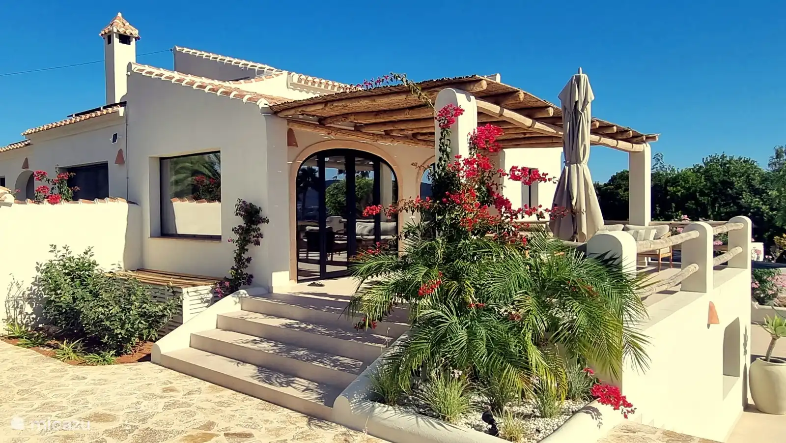 Overdekt terras met pergola en bloeiende bougainville. Hier ontbijt je in de ochtendzon en zoek je de schaduw op als het middag wordt.