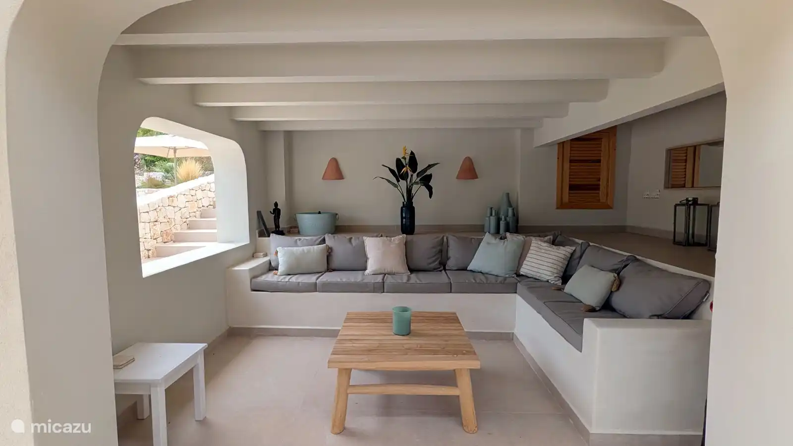 Overdekte lounge met ruime bank en uitzicht op de tuin. Een koele plek in de schaduw om te lezen, te kletsen of even niets te doen.