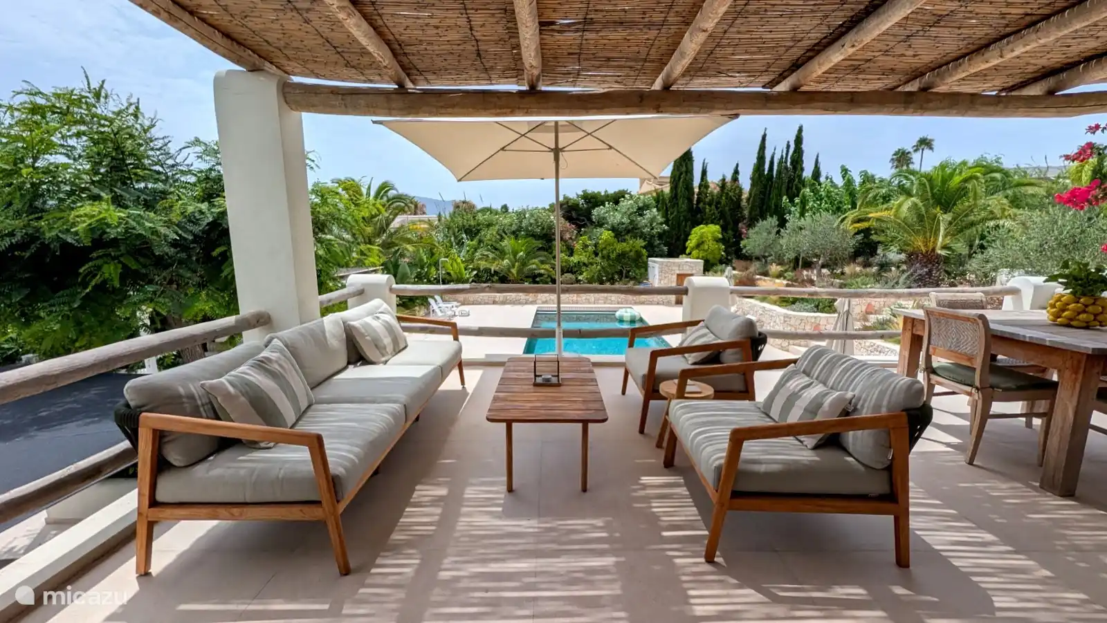 Lounge-terras onder de rieten pergola, met uitzicht op het zwembad en de tuin. De ideale plek voor een middagdutje in de schaduw.