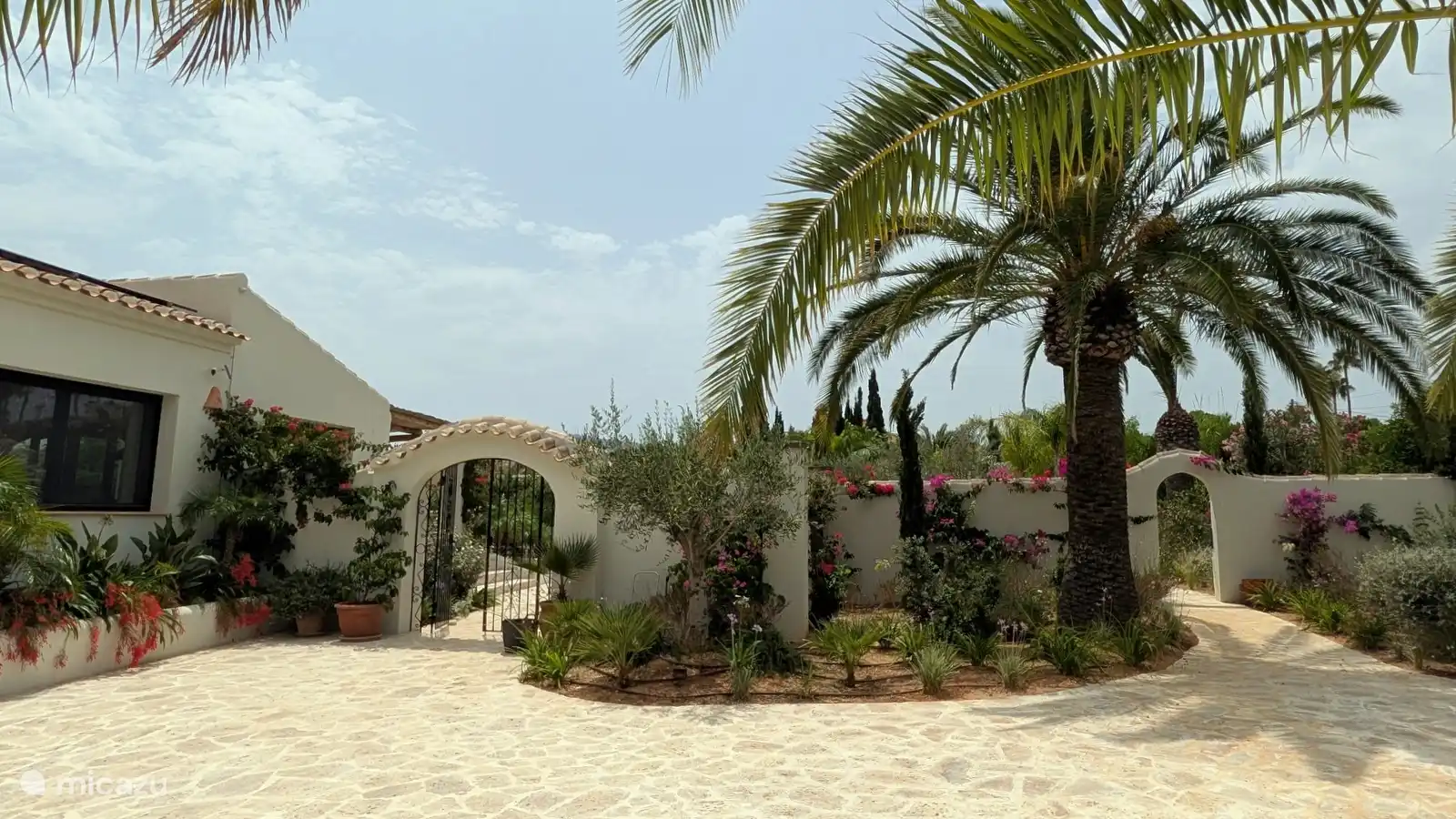 Witte muren met sierlijke bogen, palmen en bloeiende planten. De mediterrane tuin geeft je meteen dat echte Spaanse vakantiegevoel.
