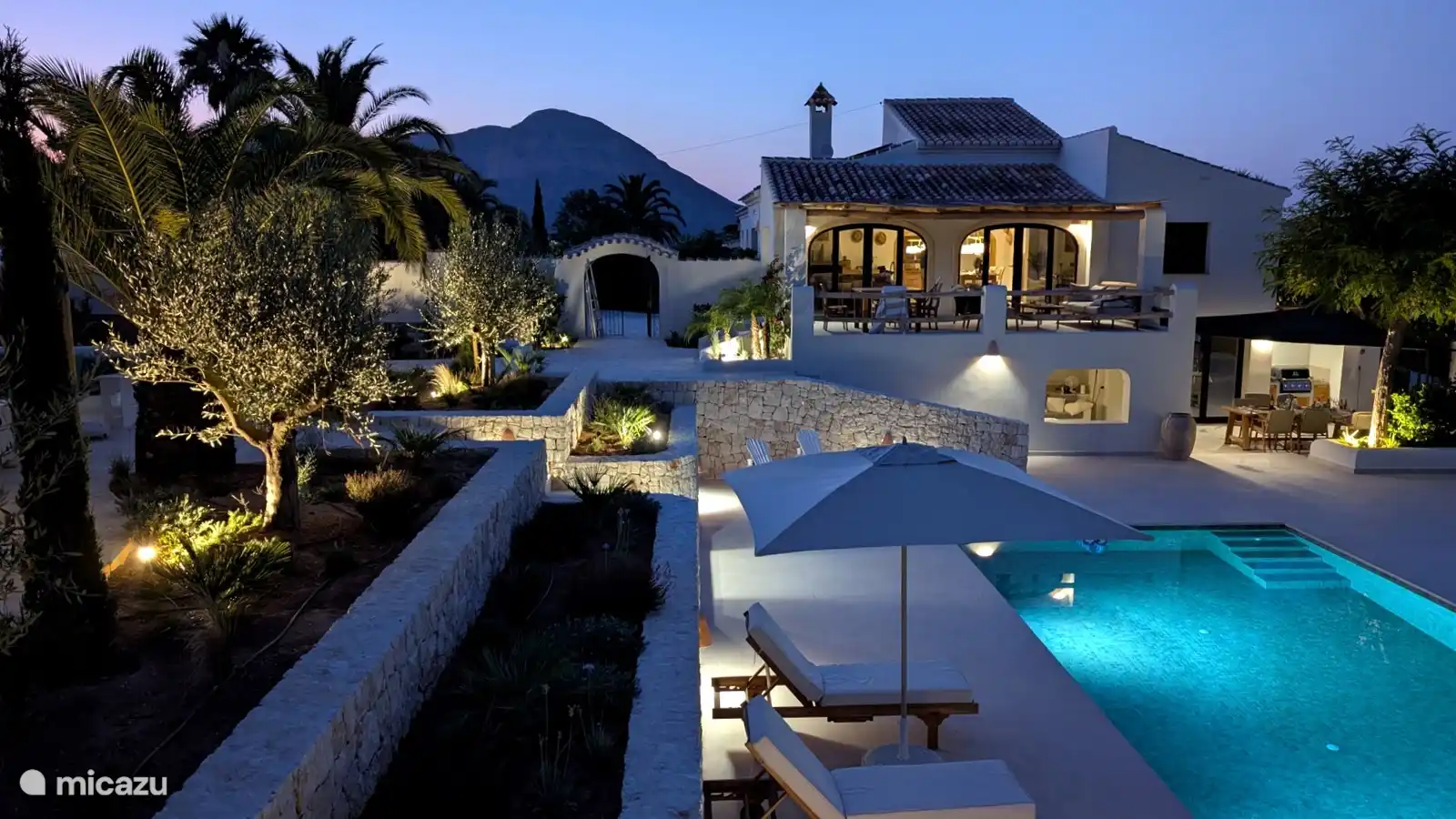 Villa, tuin en zwembad sfeervol verlicht, met de heuvels op de achtergrond. Zo sluit je elke zomerdag in stijl af.