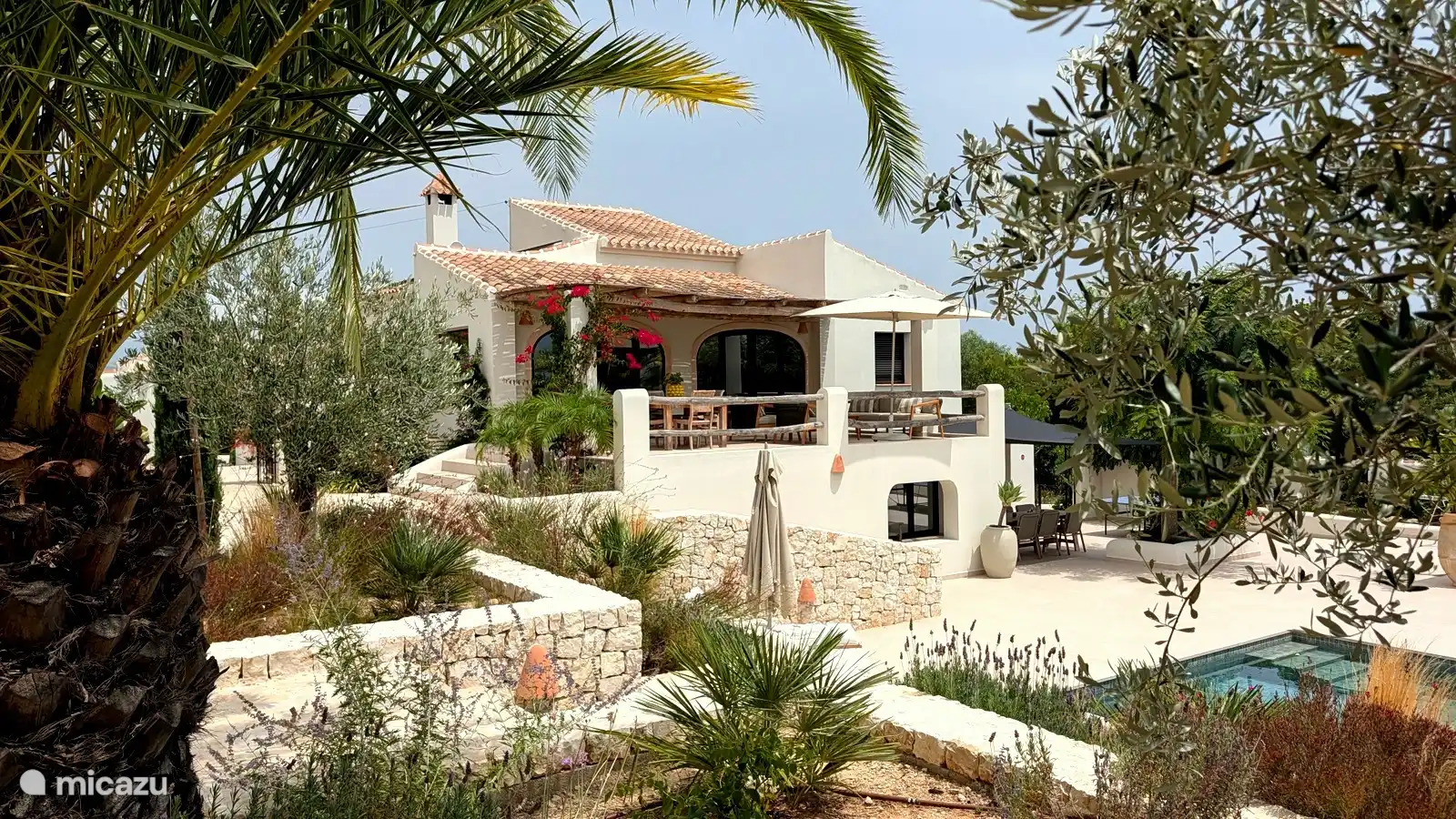 Villa gezien vanuit de tuin, met terrassen op verschillende niveaus en olijfbomen. Overal vind je een rustig plekje in de zon of juist in de schaduw.