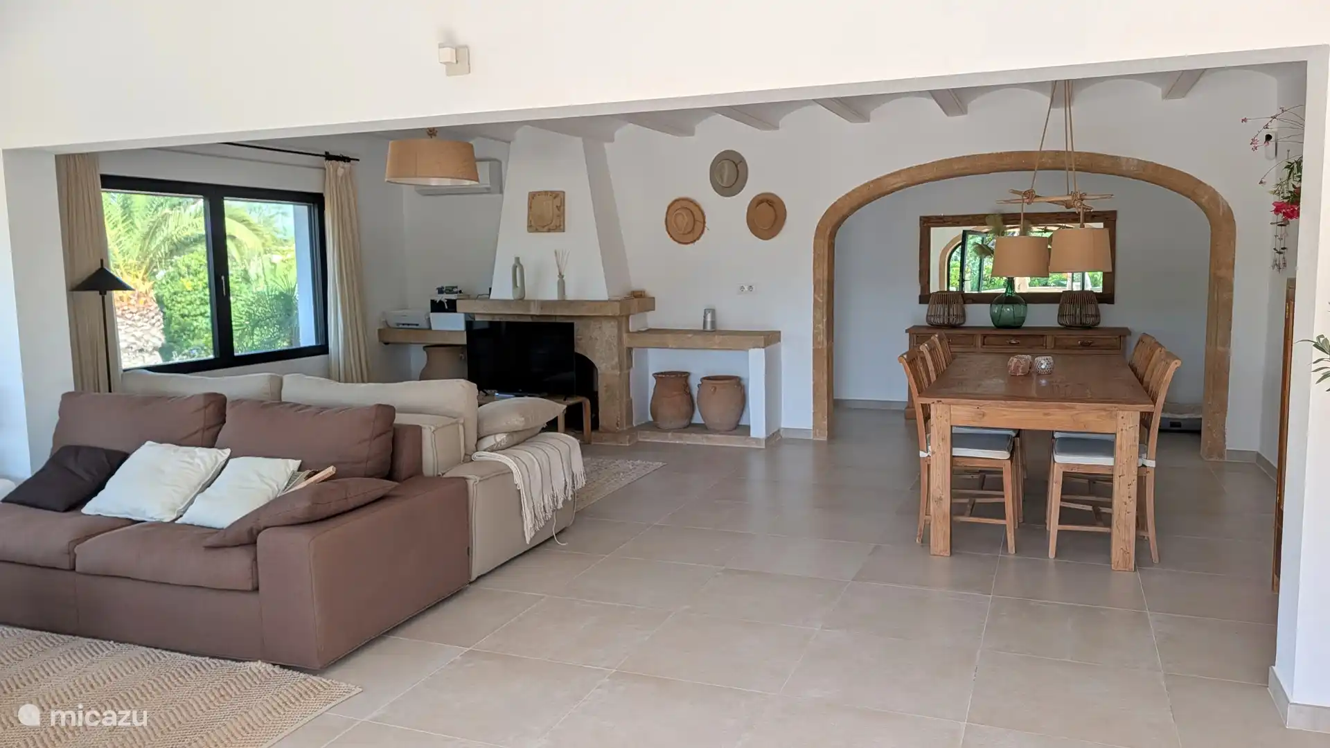 Lichte woonkamer met open haard en een ruime eethoek onder de boog. Een fijne plek om samen te eten en na een dag zon even bij te komen.