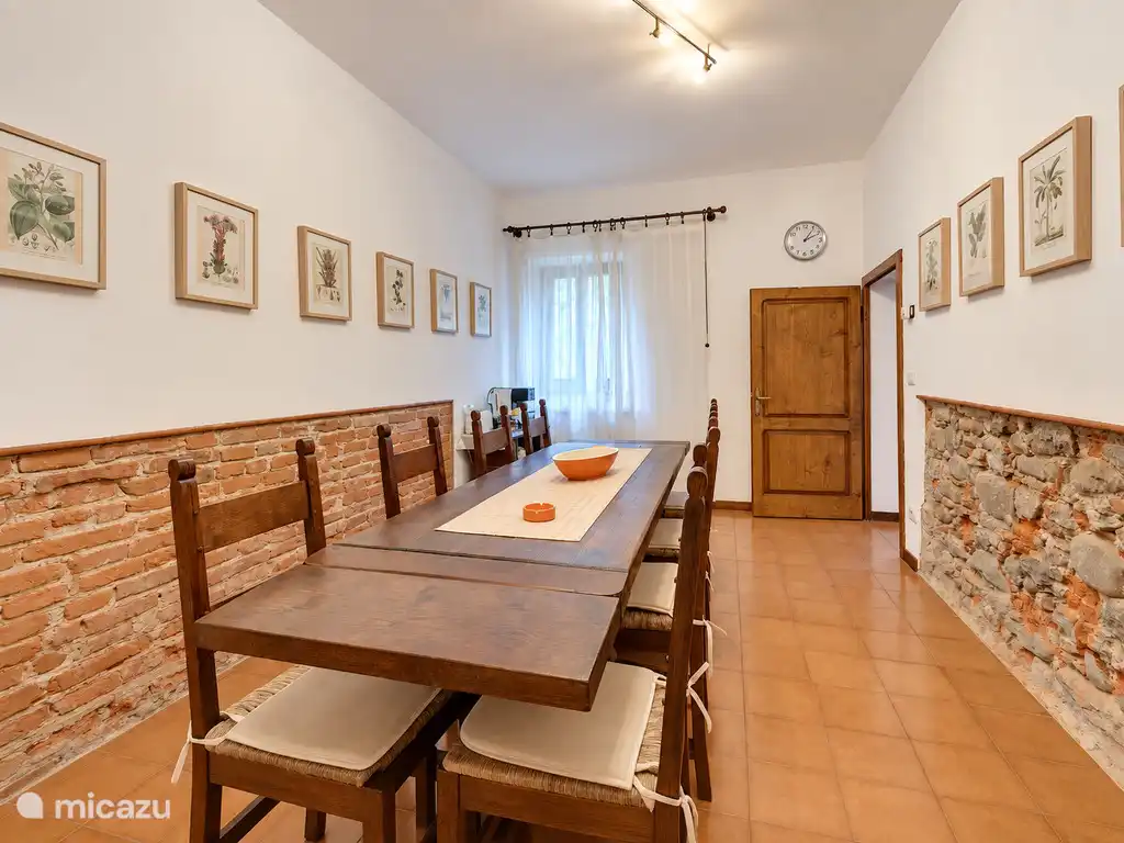 Salle à manger avec une longue table en bois, des chaises et des murs en briques et pierres apparentes.