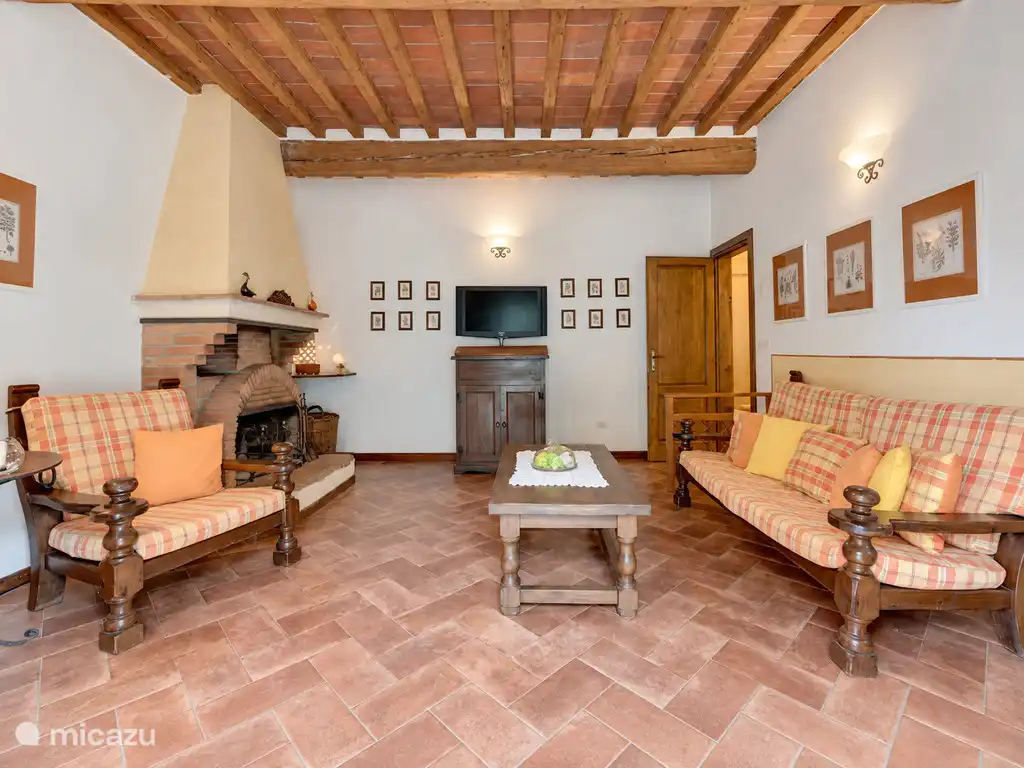Salon avec deux canapés, une cheminée, un plafond à poutres en bois et un sol en carreaux de terre cuite.