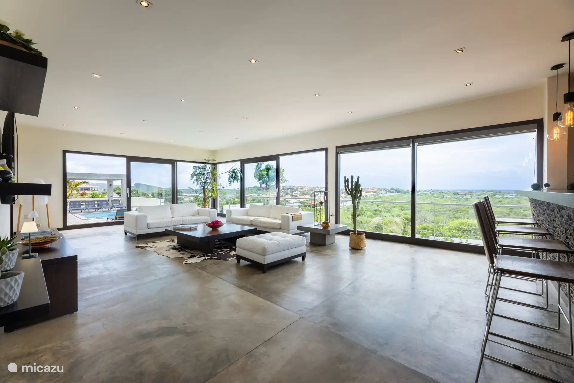 Salón espacioso con grandes ventanas/puertas correderas que difuminan la línea entre exterior y interior, ofreciendo la experiencia definitiva de vida caribeña.