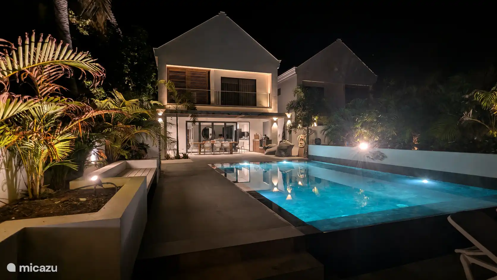 The villa at night, with the illuminated swimming pool and the covered porch.