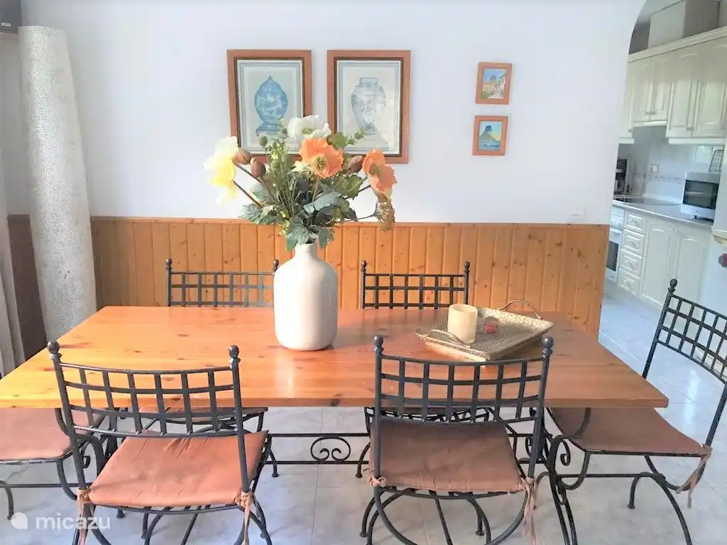 Photo d'un coin repas avec 6 chaises et vue sur le coin cuisine. Entièrement équipé avec four, micro-onde et machine à café Nespresso