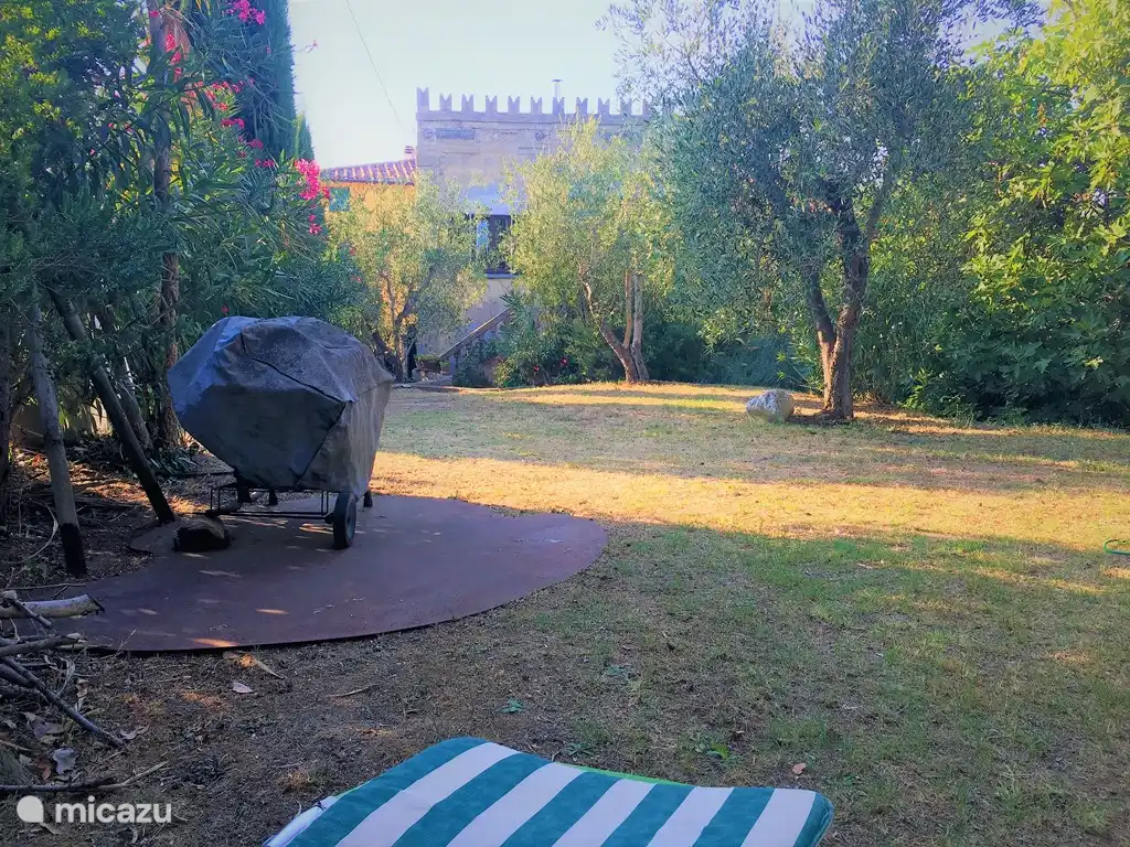 Vista desde el balcón del 1er piso sobre el jardín con vista 2ª terraza con carpa de fiesta en el límite de la propiedad, juegos para los niños entre olivos, cipreses y adelfas, bajo la higuera de 200 años, se dispone una terraza en otoño/invierno, hamacas colgantes libremente, BBQ y vista al atardecer