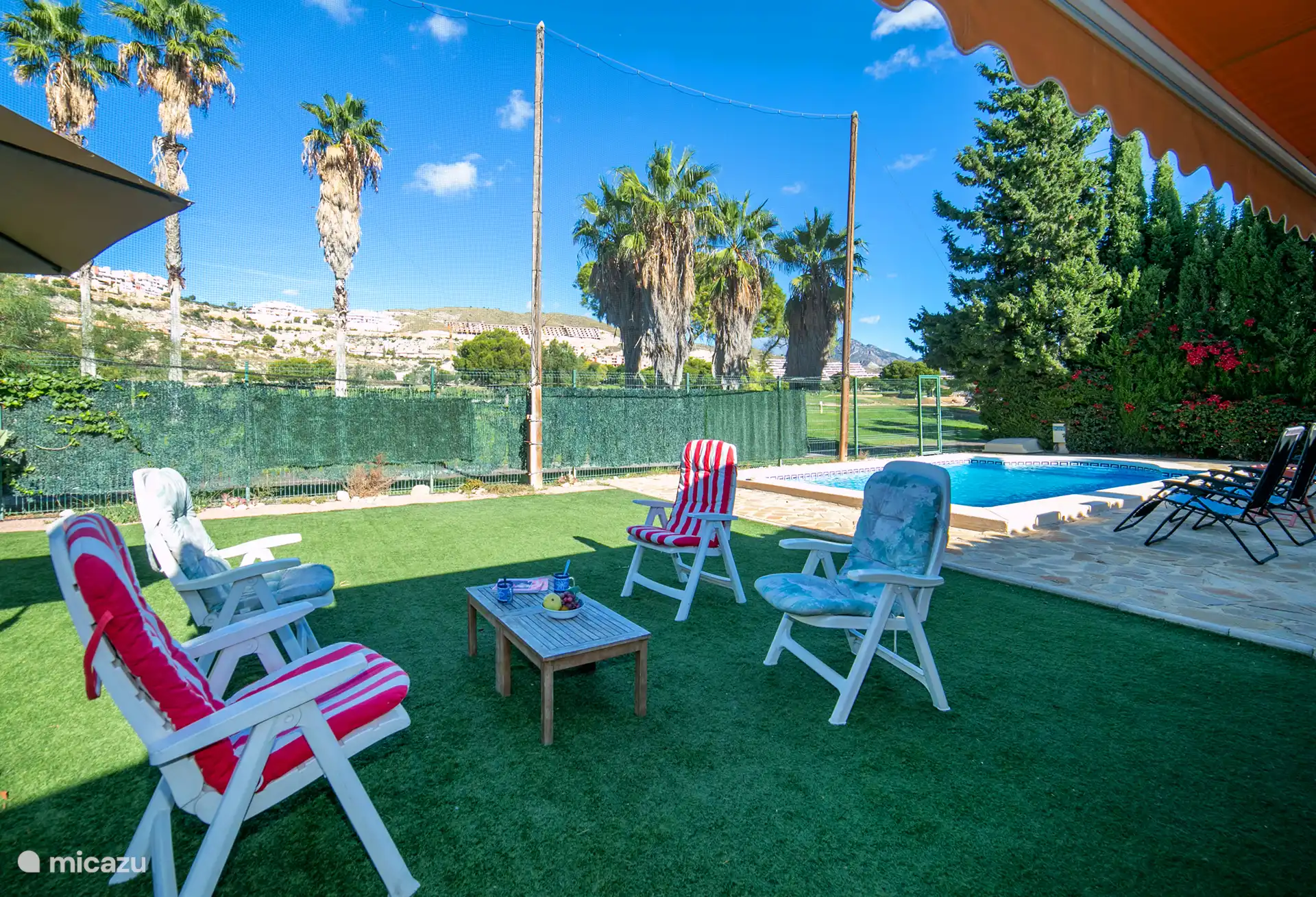 Chaises de jardin et piscine avec des transats autour.