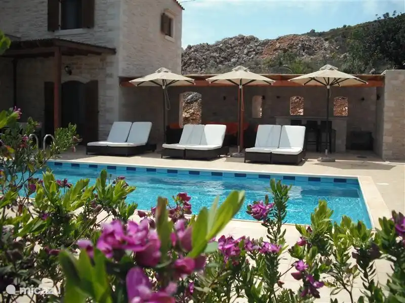 Villa de luxe avec une grande terrasse ensoleillée avec des chaises longues de luxe, un ensemble de salons et un bar de piscine avec réfrigérateur.