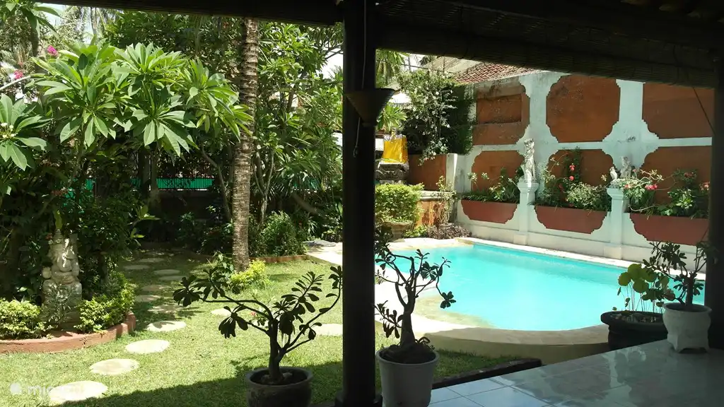 Blick von der überdachten Terrasse (mit einer Decke) auf den Pool und Garten.