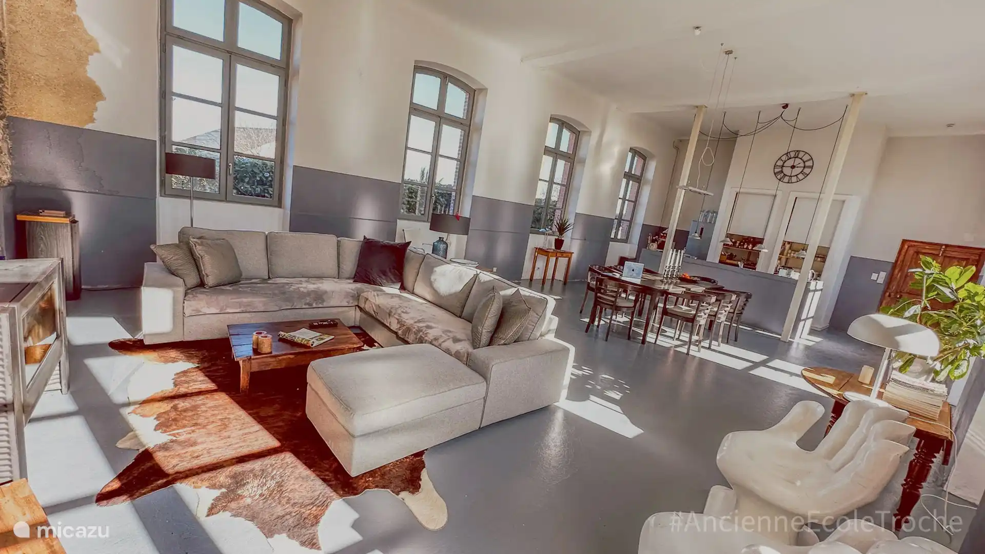 Der großzügige Wohnraum. Zu sehen ist der Ess- und Sitzbereich, rechts die Kücheninsel. Hohe Fenster und Türen geben den Blick auf den grünen Garten frei. 