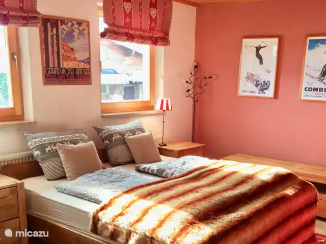 Va et Vient Zell am See/Kaprun en Austria, Salzburgo, Kaprun - chalet Una de las dos habitaciones dobles (dormitorio principal) de la planta baja vista desde el otro lado. Junto a la pared roja se encuentra la entrada al cuarto de baño privado con lavabo y WC.