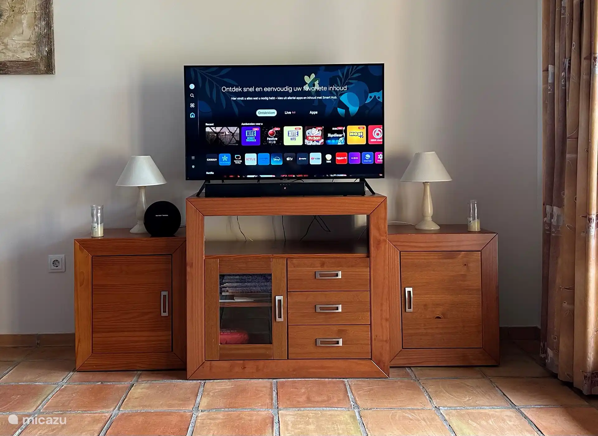 Unidad de pared con Smart TV de pantalla plana, barra de sonido y altavoz (bluetooth).  El mobiliario contiene juegos, manuales e información sobre la zona.