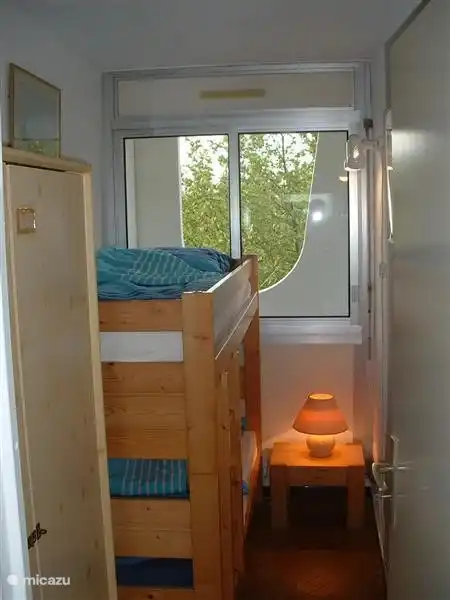 Kinderkamer met stapelbed en raam met rolluik. Uitzicht op overdekt balkon achter en op park.