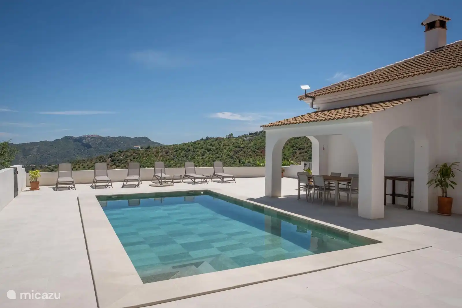 Groot terras met zon- en schaduwplekken rondom schitterende zwembad