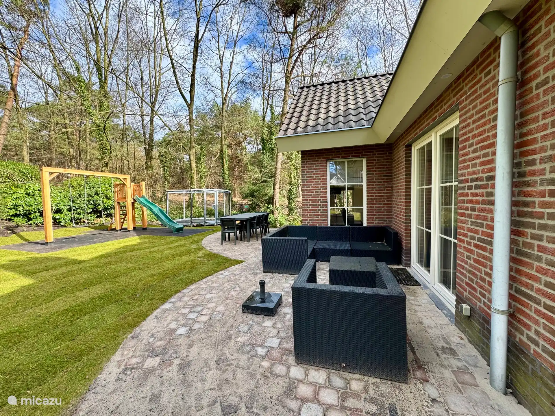 De achterzijde van de vakantiewoning met speeltoestel en trampoline.