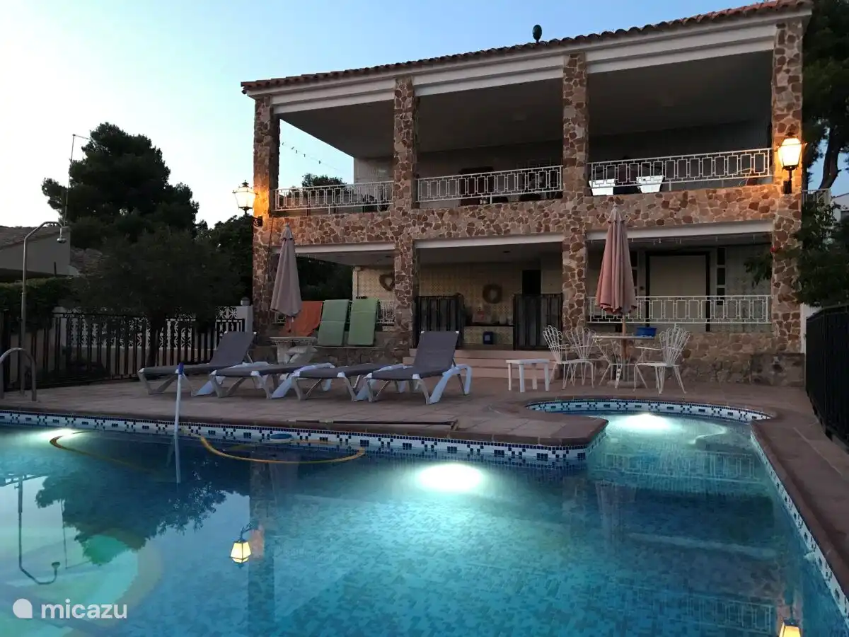 Mit beleuchtetem Pool am Abend und großen Veranden