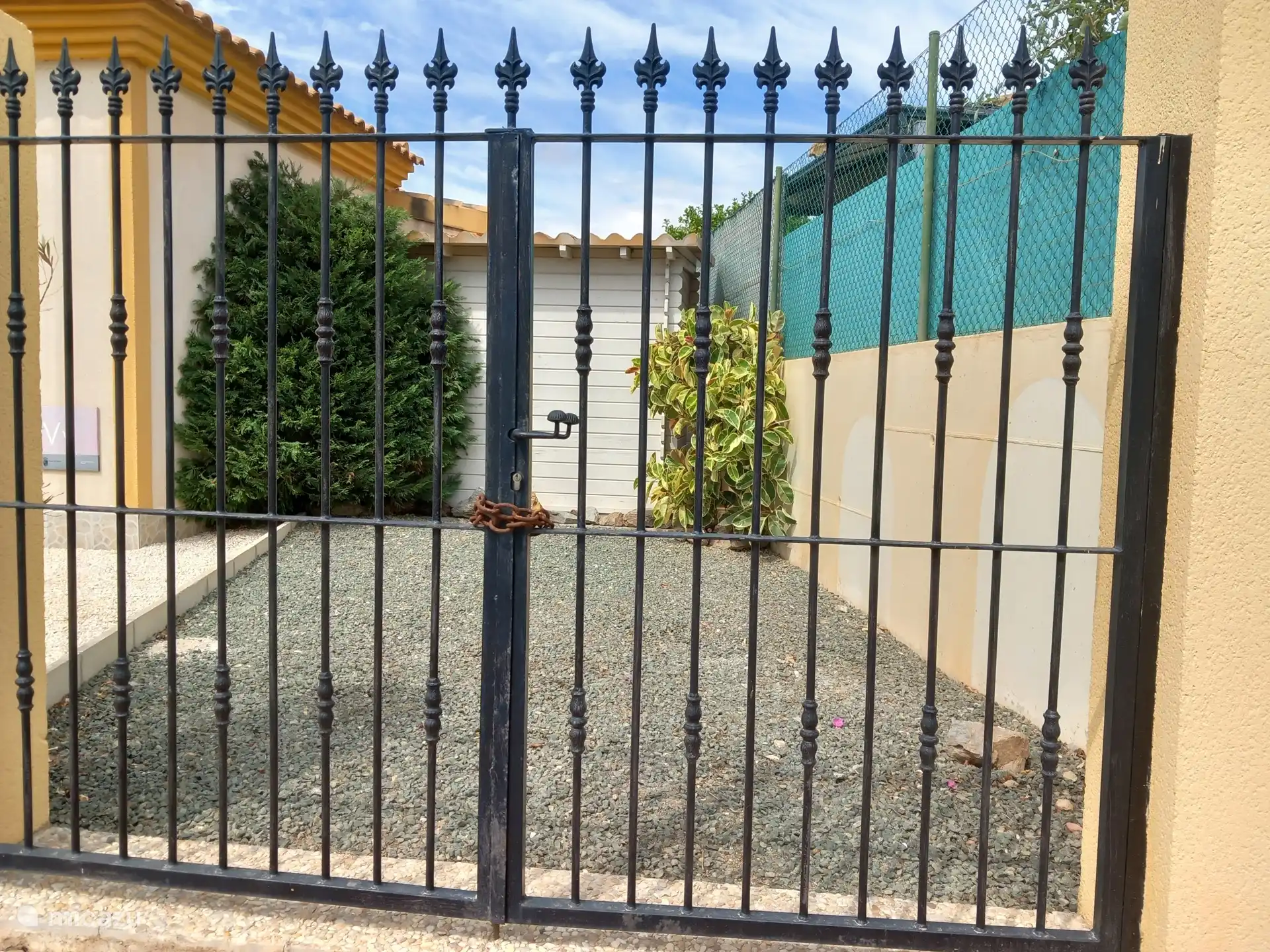 Rückseite des Abstellraums/Gartenhauses und Parkplatz, von der Straße aus gesehen. Nadel- und Ficusbäume wachsen kräftig. Zweimal jährlich zu schneiden ist immer notwendig.