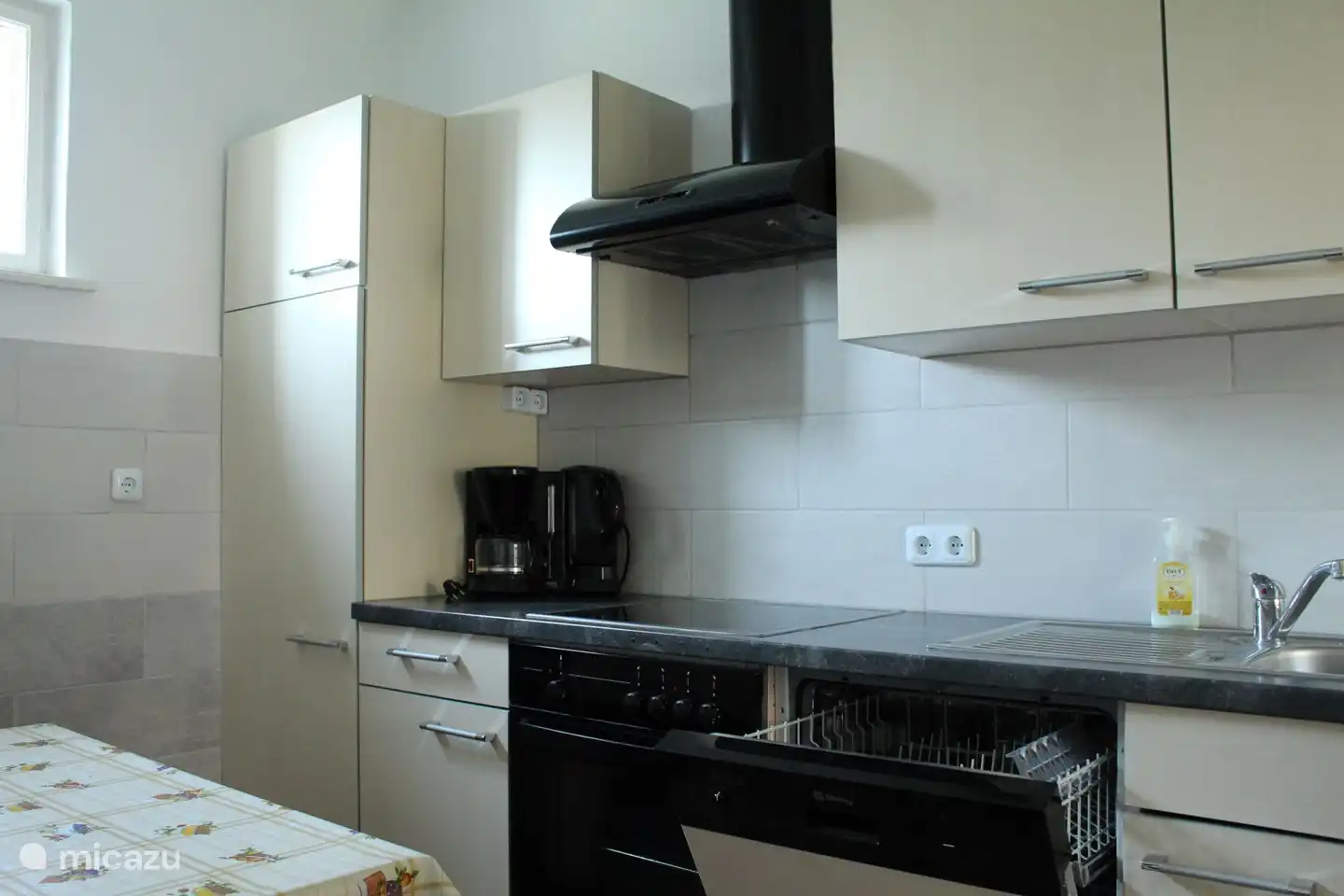 Küchenzeile mit Spülmaschine, Ceran-Kochfeld Kühlschrank, Gefrierfach, Kaffeemaschine und Wasserkocher.