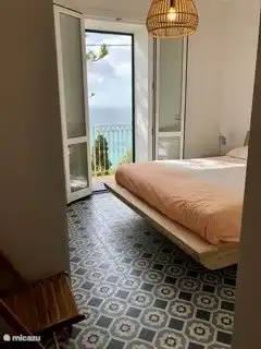 Chambre bleue avec un lit double et des portes-fenêtres donnant sur le balcon.